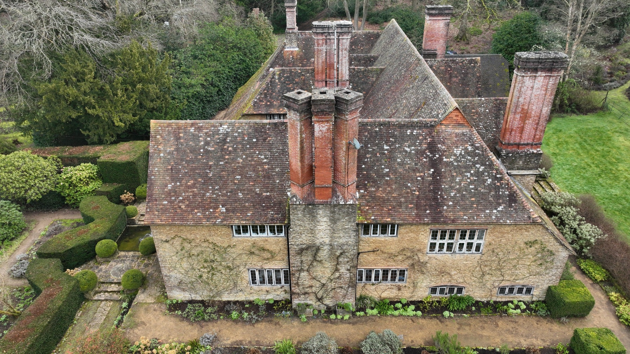 Aerial view showing a large roofscape with many ornate brick chimneys of differing heights.