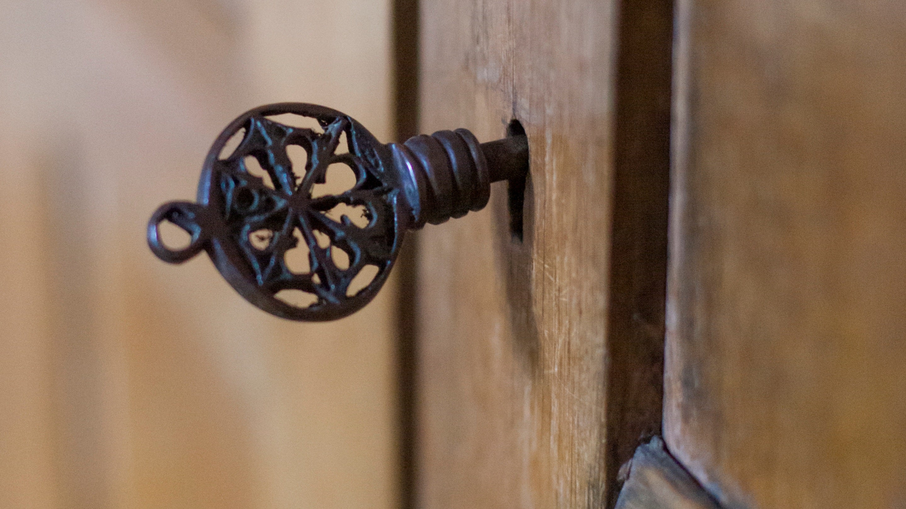 A metal key in a door lock.  The key is handmade in the design of a flower or church window.  Munstead Wood, Surrey.