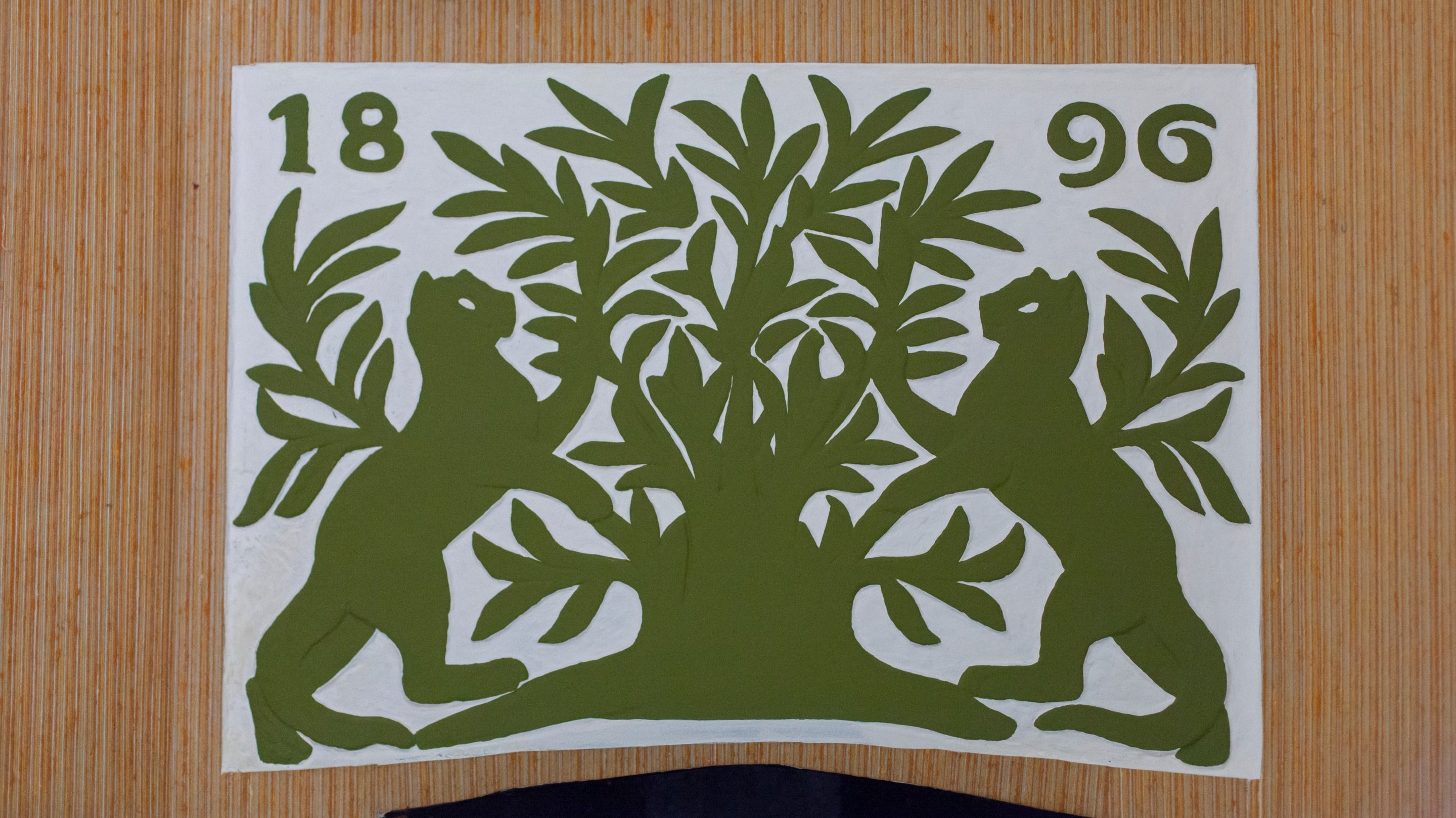 Decorative panel above the fireplace in the dressing room at Munstead Wood, Surrey.  Made by Gertrude Jekyll, two cats stand either side of a tree, painted green on a white background.  The date of the house, 1896, is carved above.