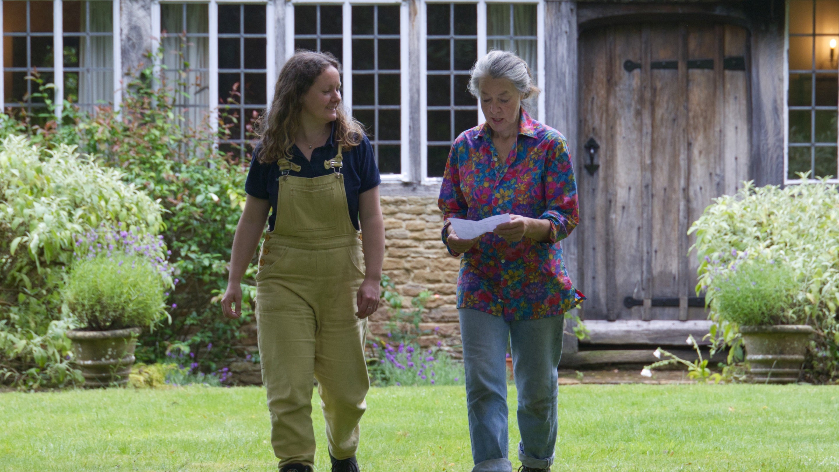 Two gardeners walking across a lawn in front of a house