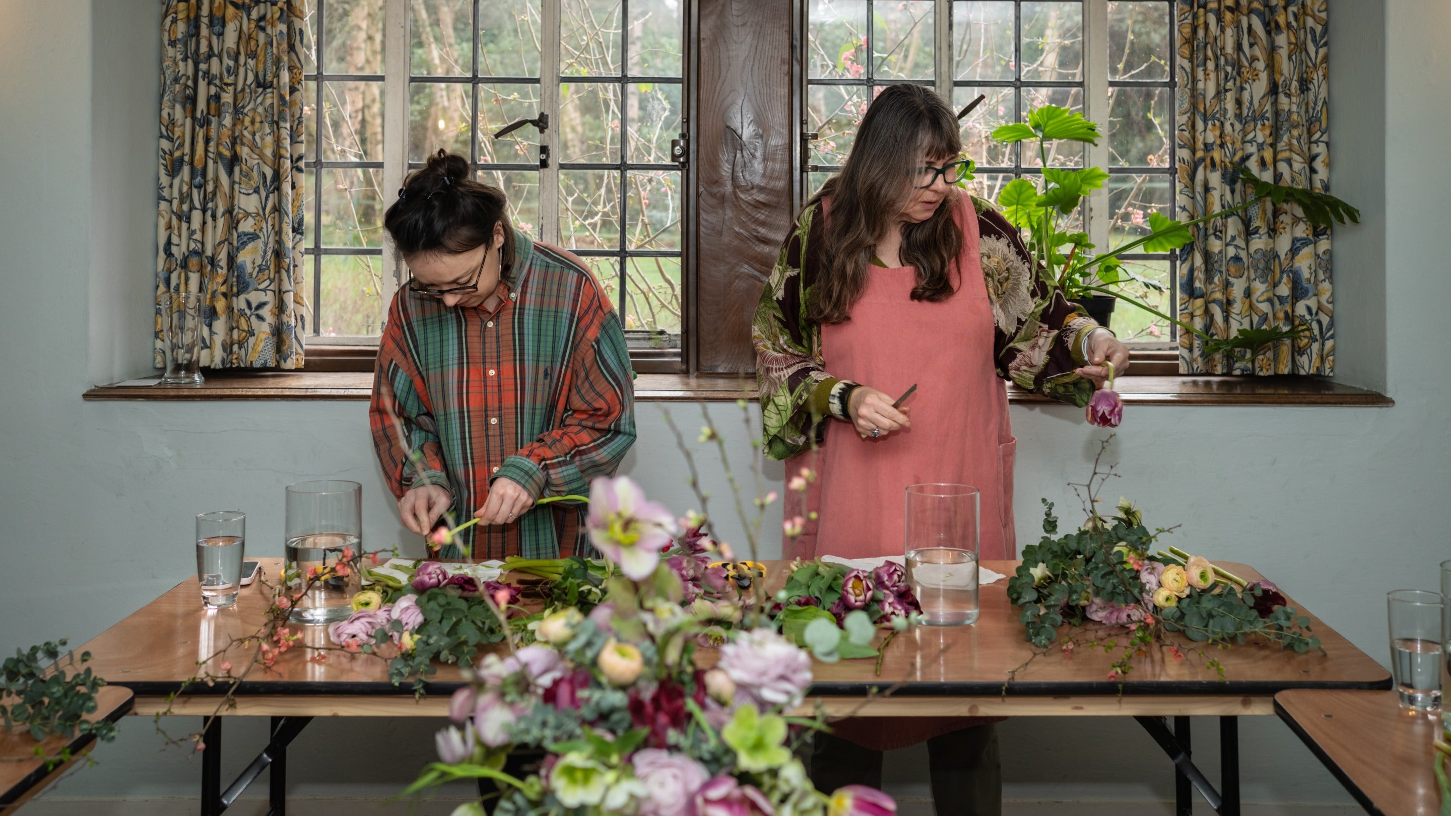 Two people arranging flowers with vase of flowers in foreground