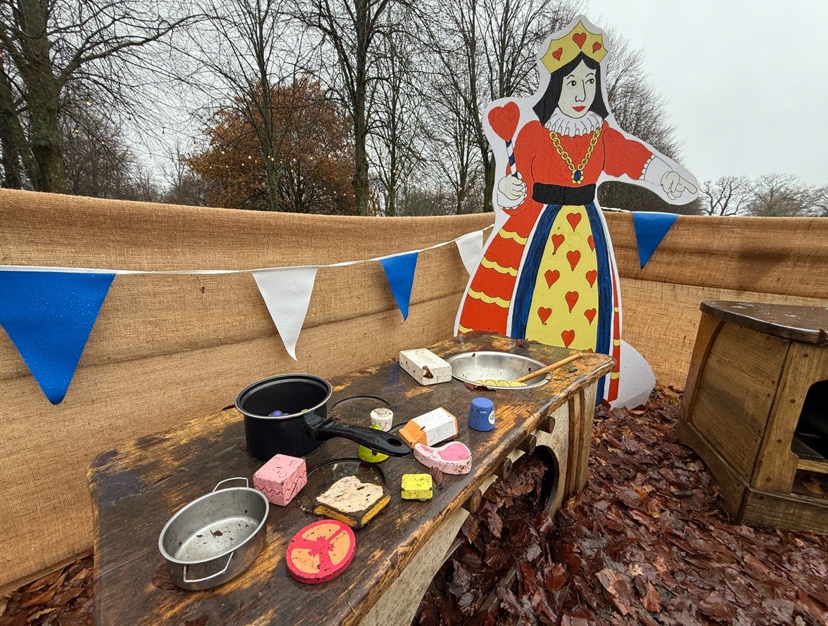 Alice's Christmas in Wonderland at Polesden Lacey 2025 - an outdoor play area for toddlers with a play kitchen, blue and white bunting and life-size picture of the Queen of Hearts