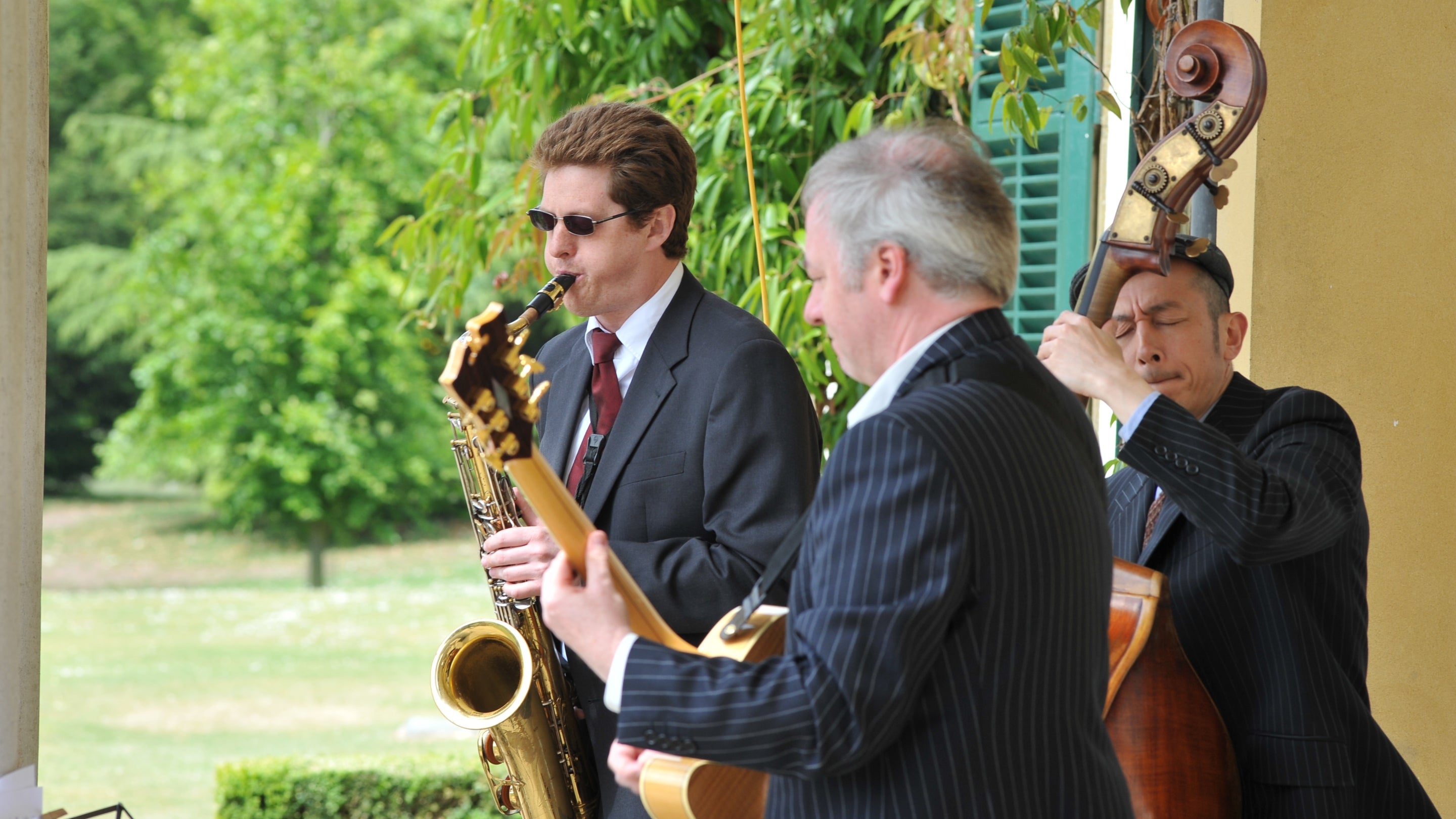 Three jazz musicians in suits playing instruments in the sunshine at Polesden Lacey