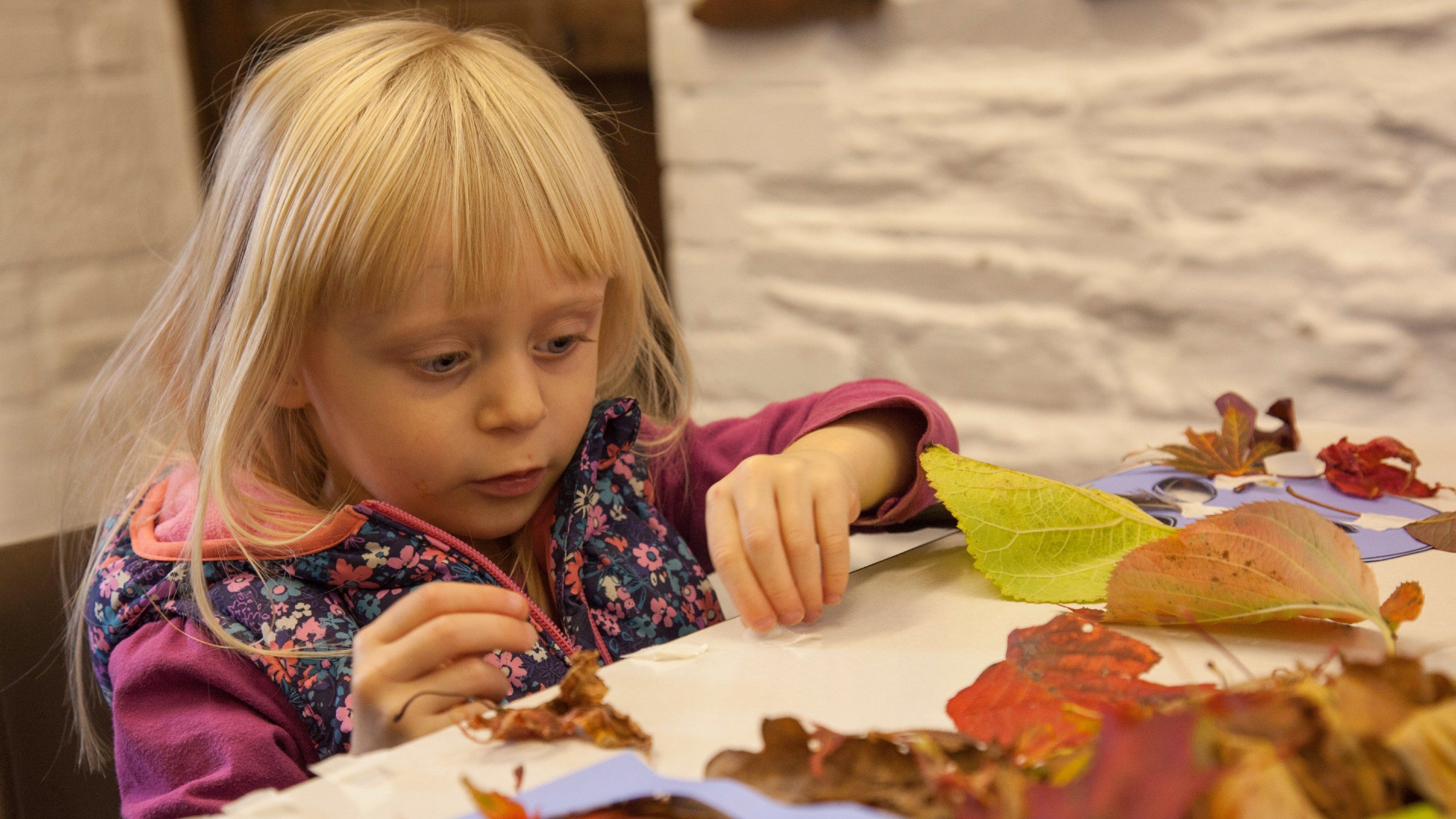 Girl sitting at a table with autumn crafts including leaves and glue