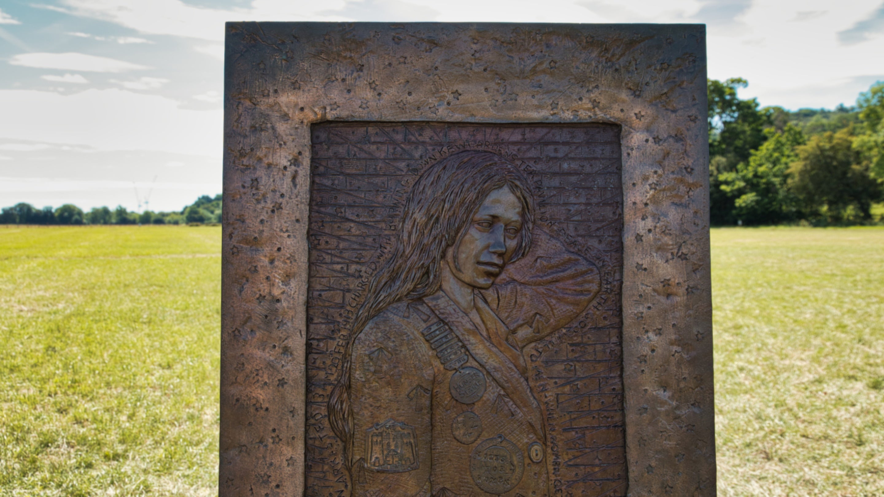 Close-up of chair 1 of The Jurors by Hew Locke, on display at Runnymede, Surrey: showing a woman in a jacket with badges, who is the suffragette Lillie Lenton
