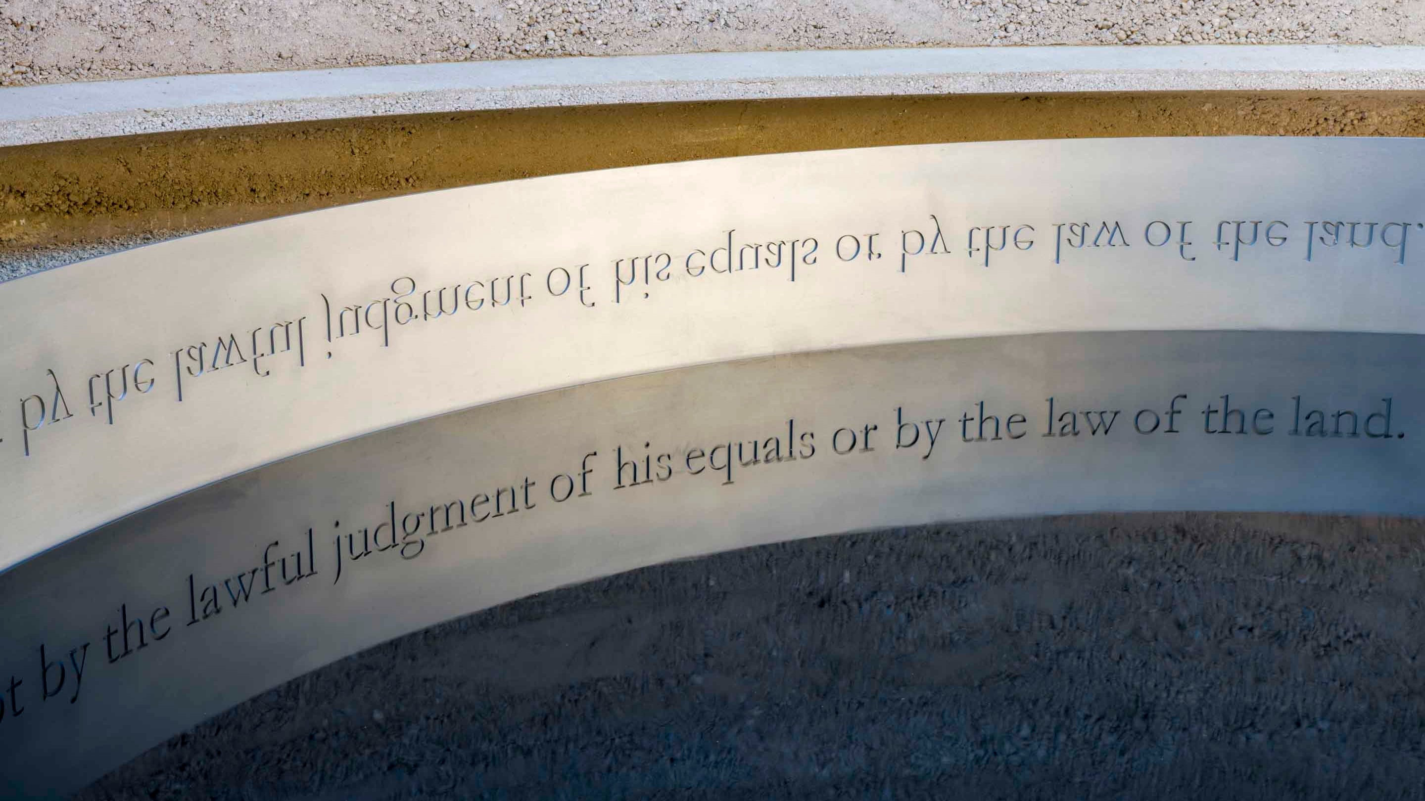 The carved words of the artwork 'Writ in Water', by Mark Wallinger, reflected in the water, at Runnymede, Surrey