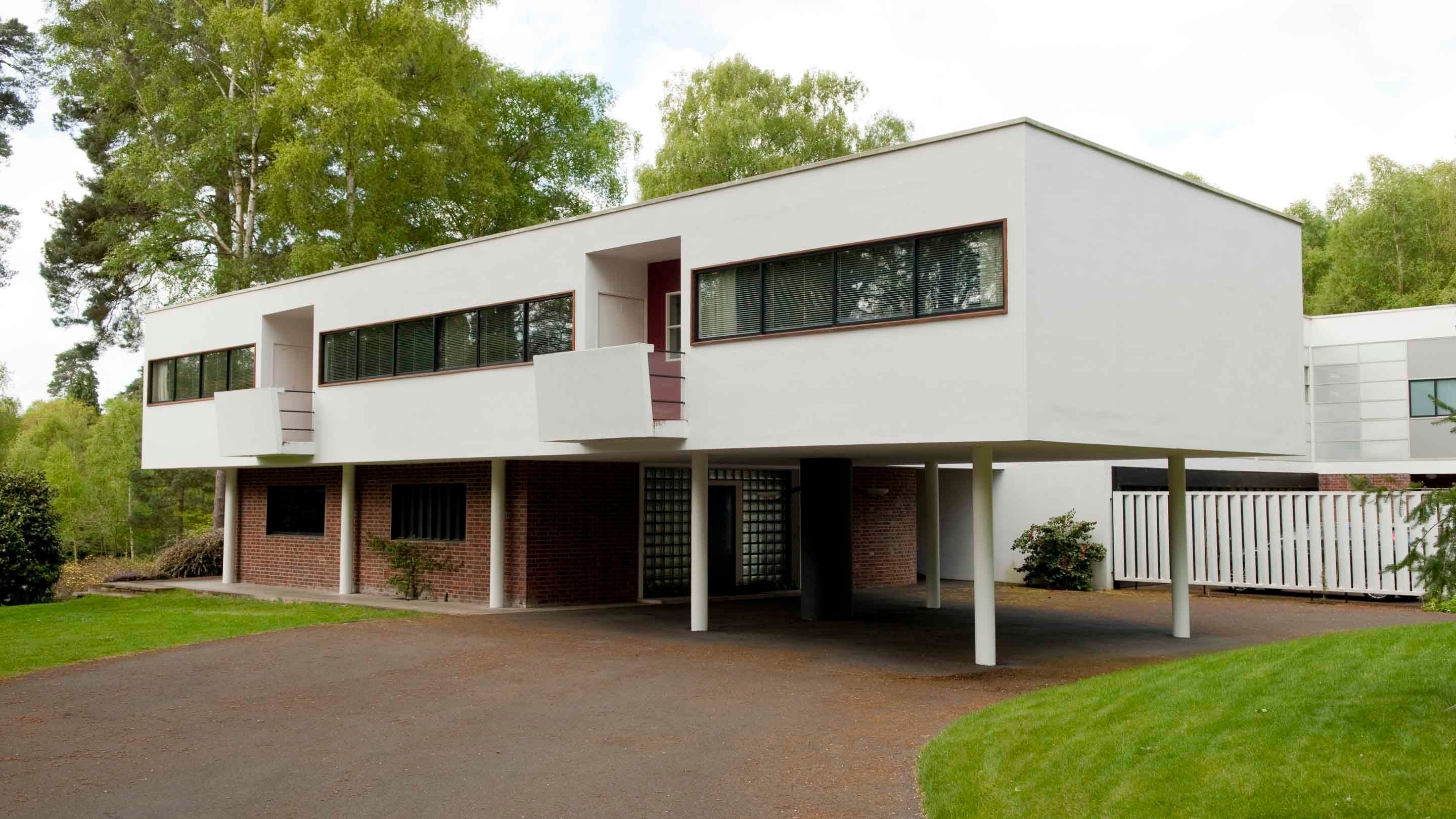 External view of The Homewood, Surrey. A smaller brick builder with a large white angular first storey above, suspended on white columns with a row of windows along the front.