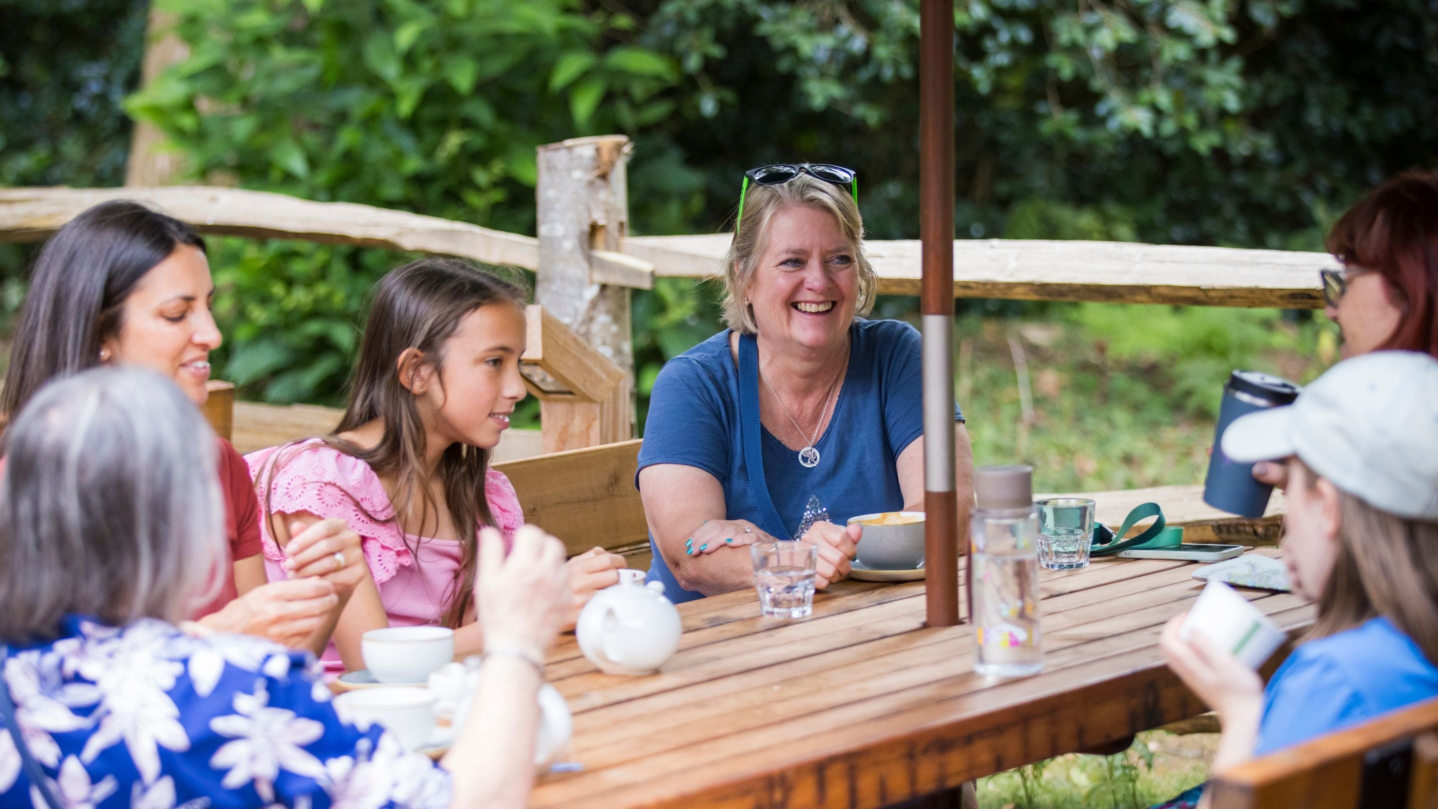 Visitors chatting and having drinks around an outside cafe table at Winkworth Arboretum