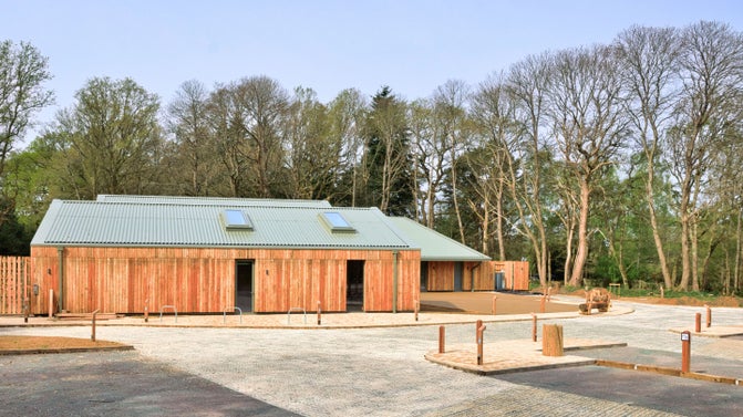 Winkworth's new visitor centre detailing a single story wooden building clad in larch timber giving a natural rustic appearance, In the foreground is the car park.