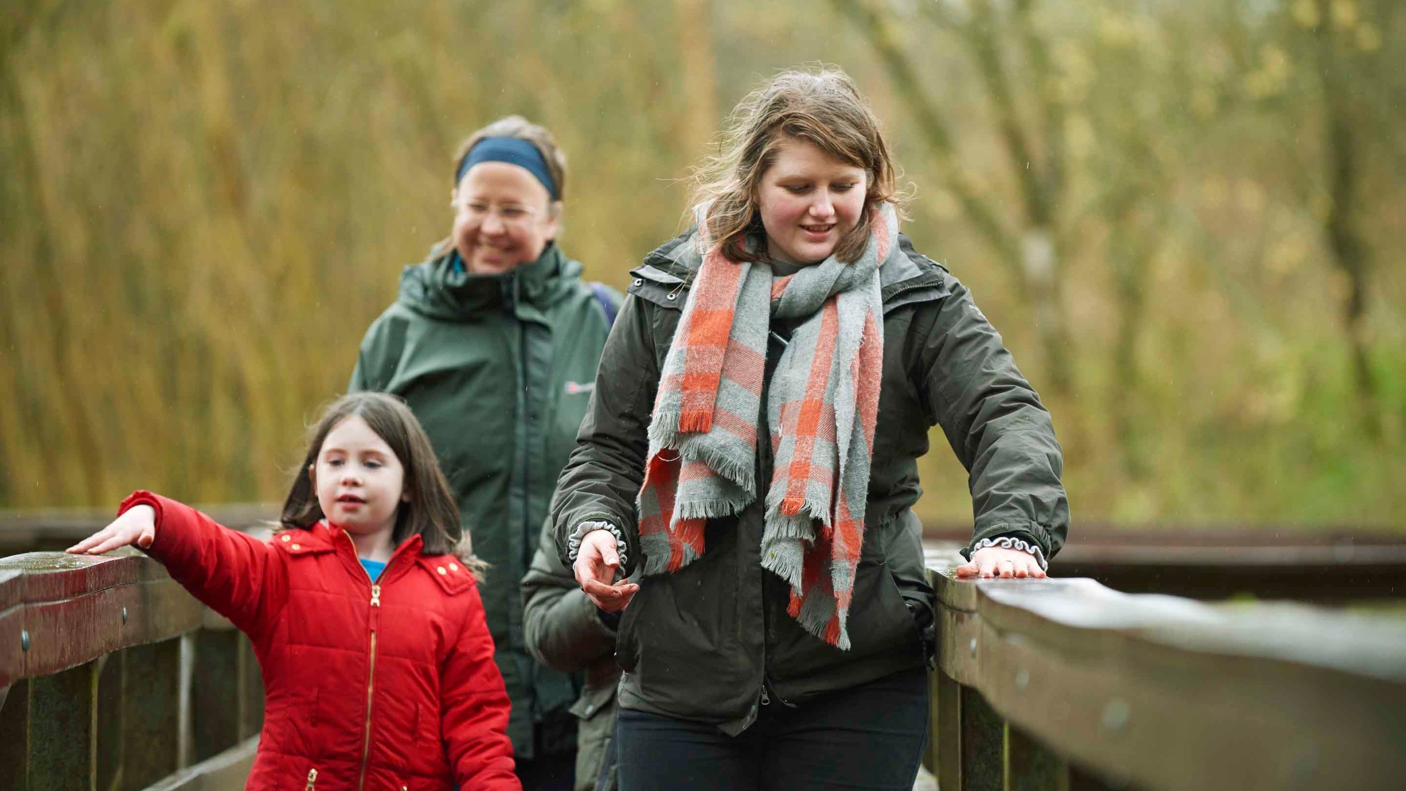 A family are crossing a sturdy wooden bridge at Winkworth Arboretum, Surrey, and there are trees in soft focus in the background.
