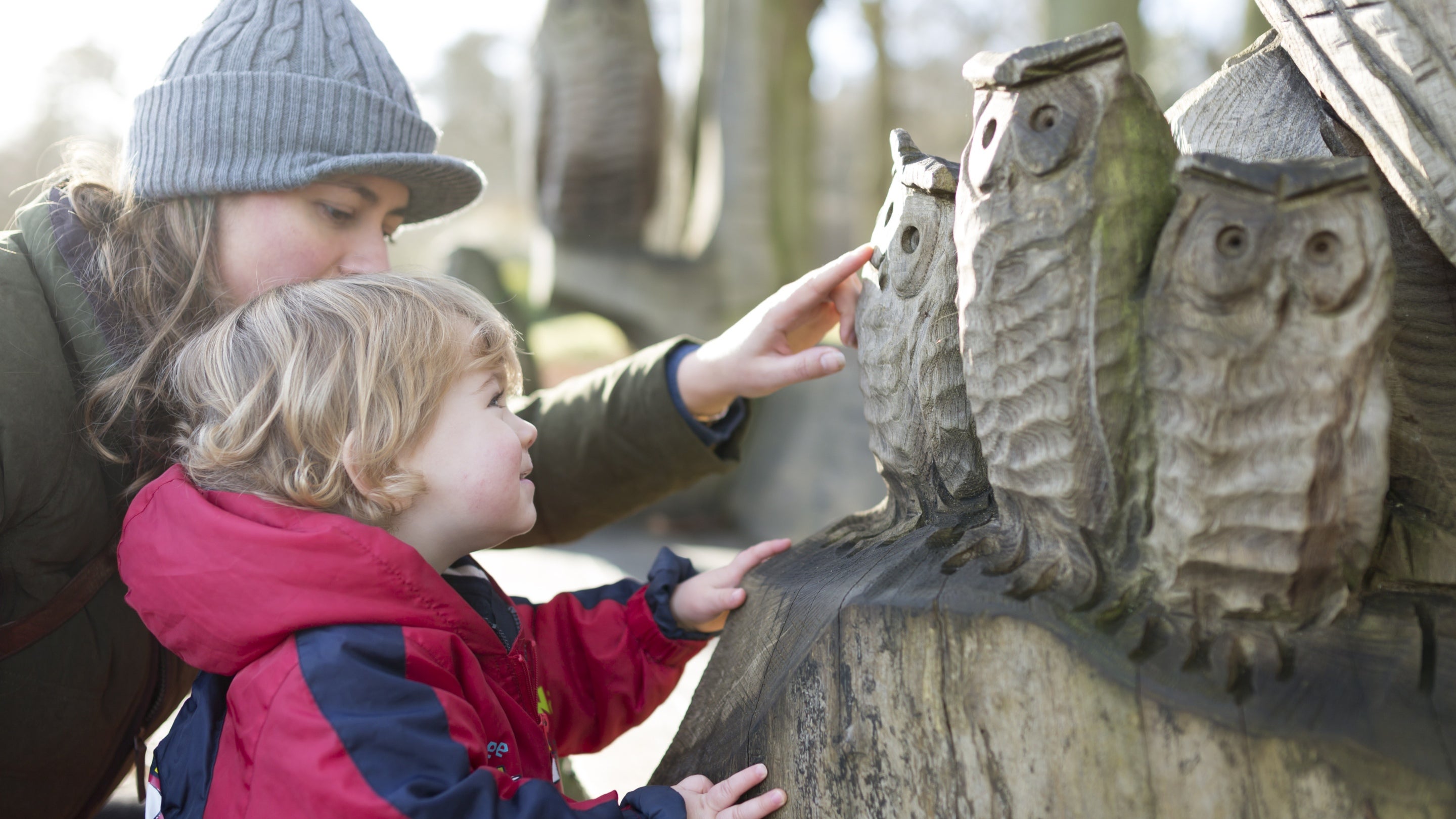 Visiting family members admiring a wooden owl sculpture on a winter's day at Winkworth Arboretum, Surrey