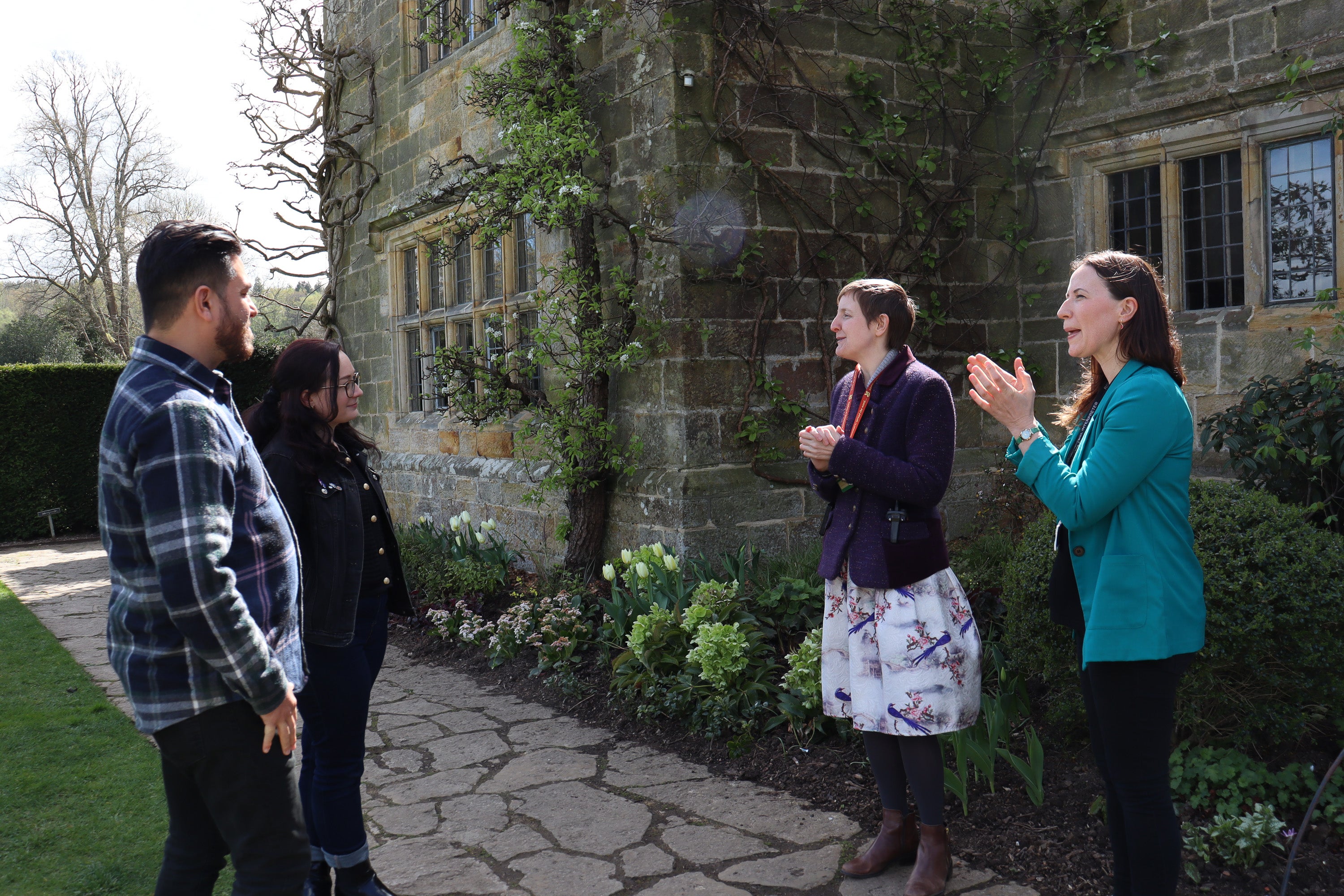 Four people standing outside a stone building, engaged in conversation. One of them is demonstrating British Sign Language.