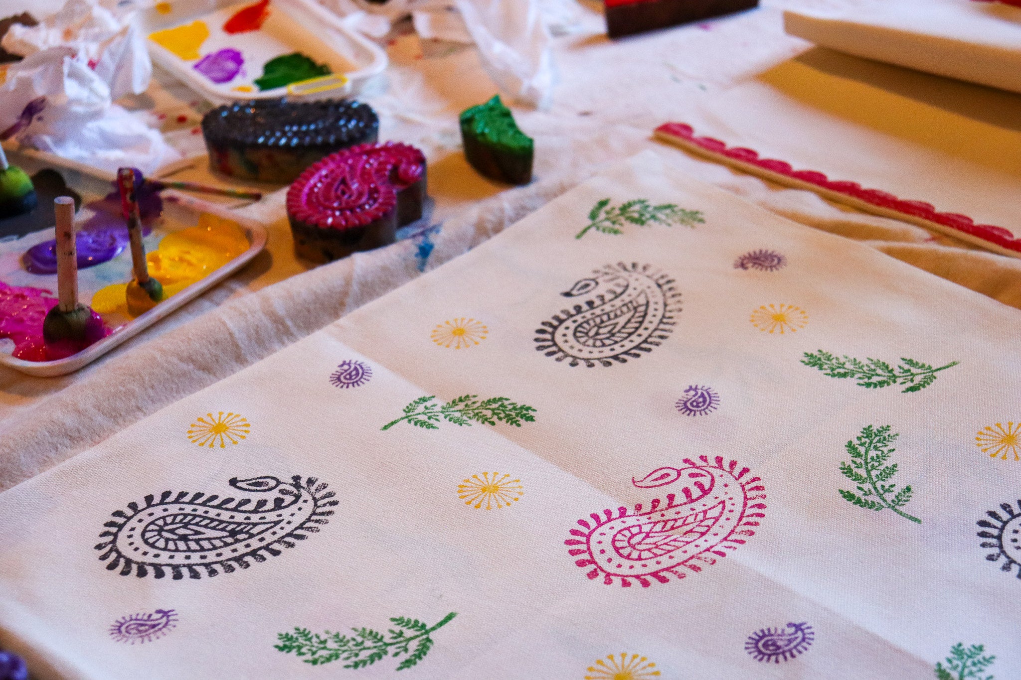 Woodblock prints being used to print colourful paints onto a piece of fabric