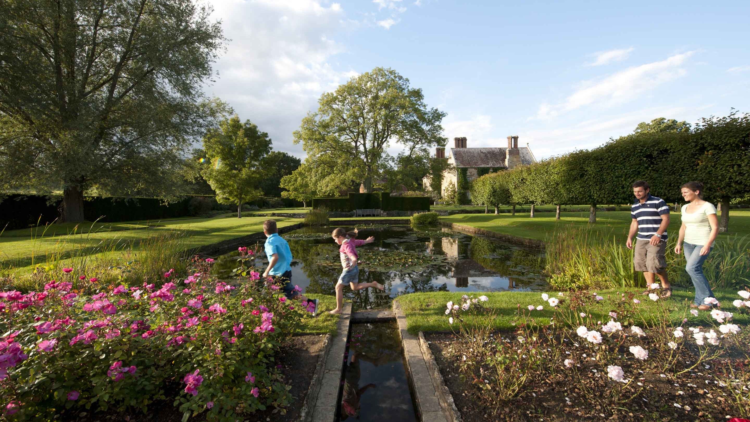 A family strolling across the top of the rectangular pond at Bateman's with the rose garden in the foreground