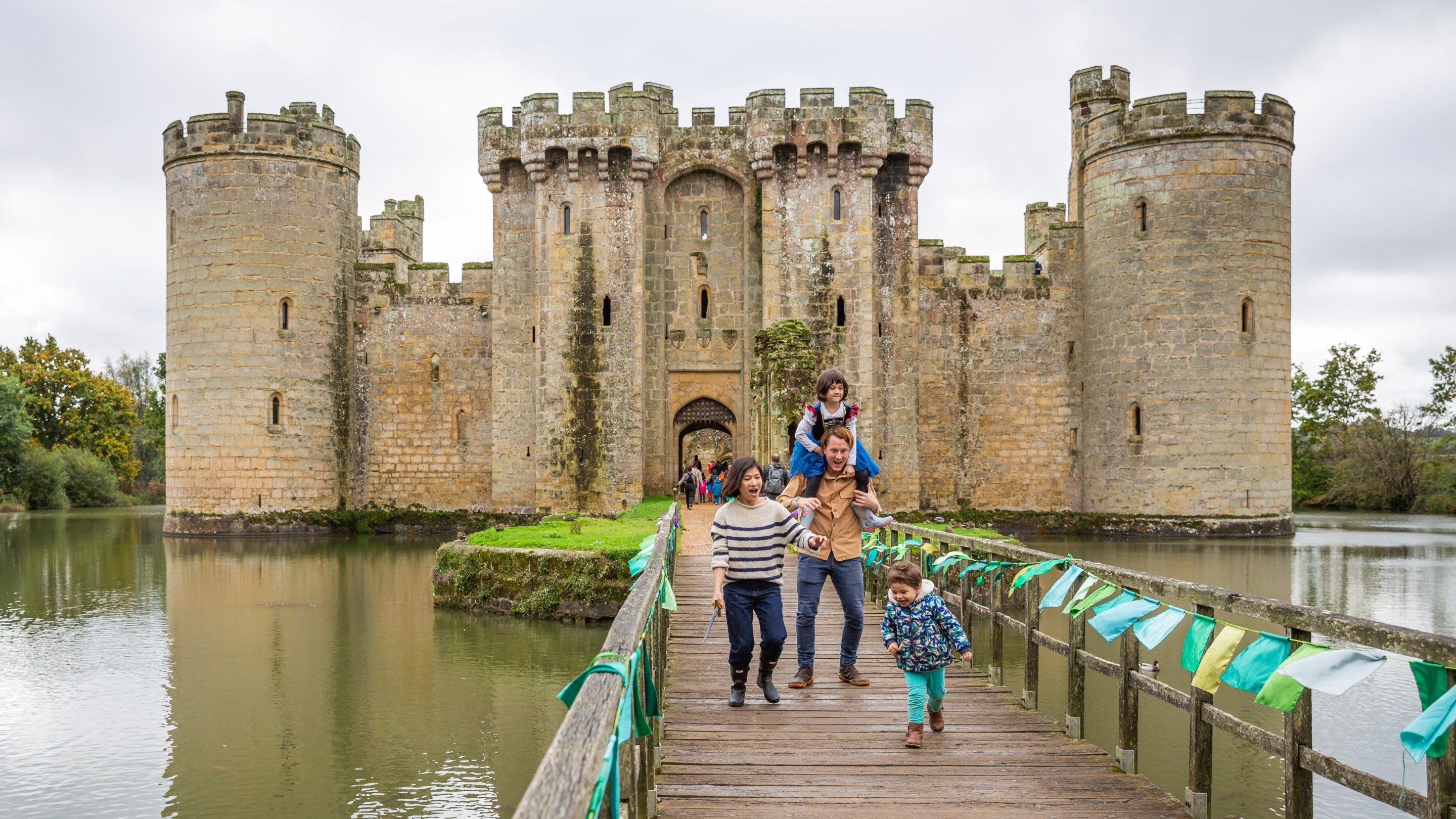 A family cross a bridge towards the camera with a castle behind them