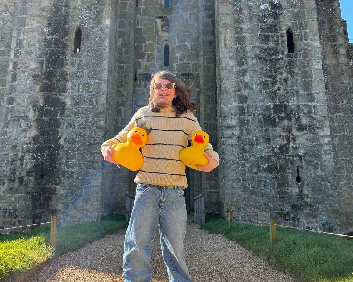 A person holding a giant rubber yellow duck outside the castle gate.