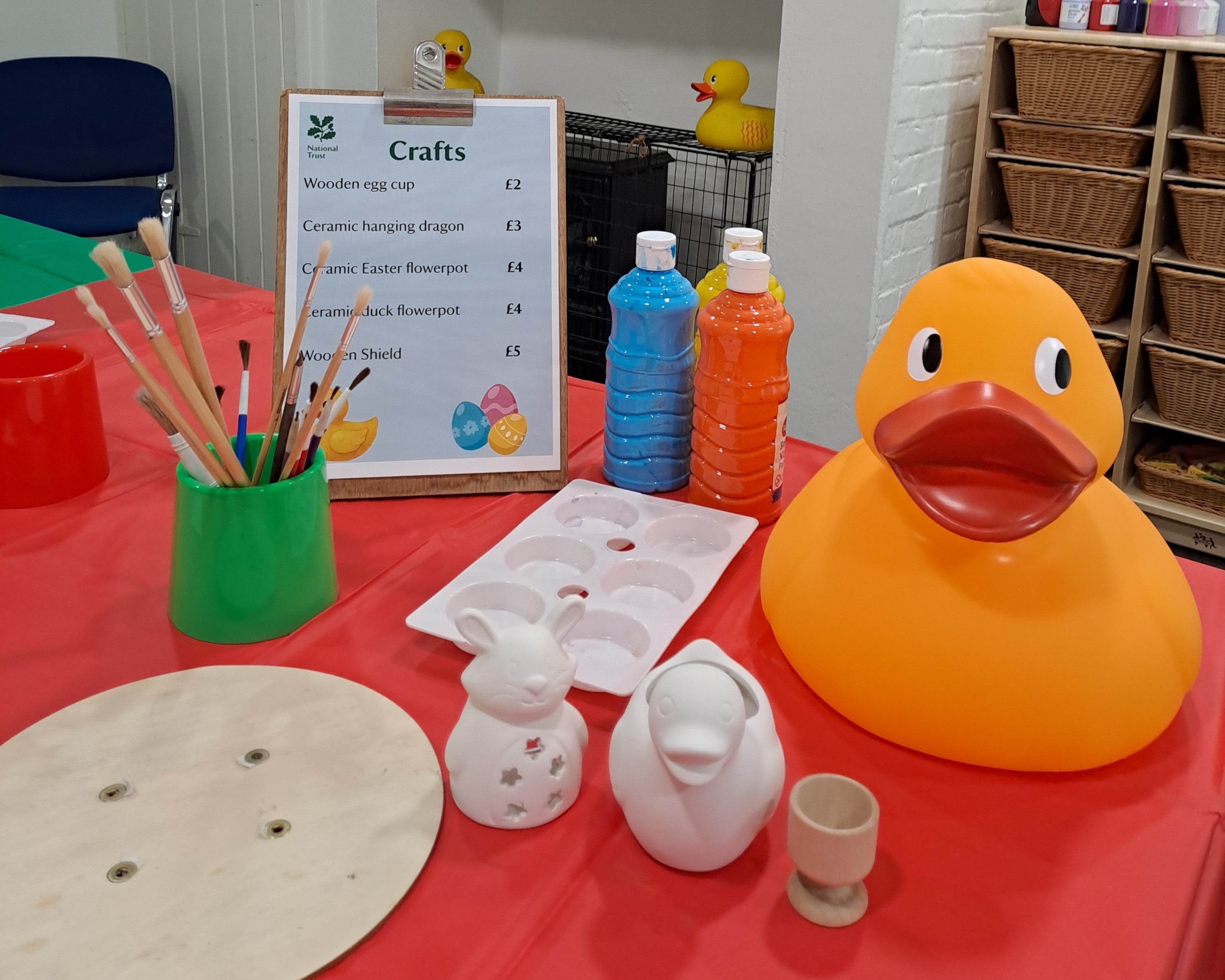 A table laid out with paint, paint brushes, wooden shields and ceramic animals to paint.