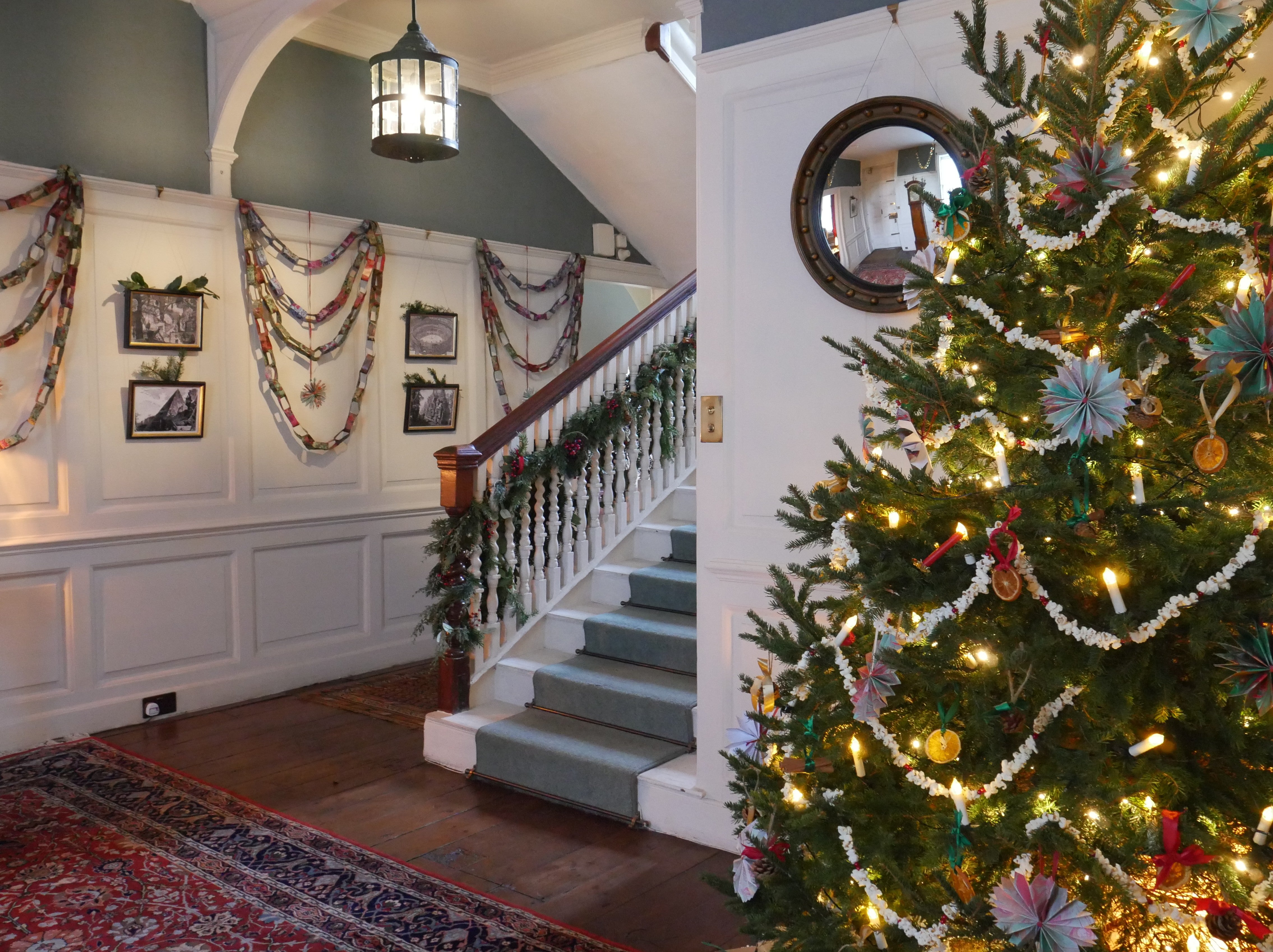 A decorated Christmas tree stands on the far right-hand side of the screen, with a decorated staircase and walls in the background