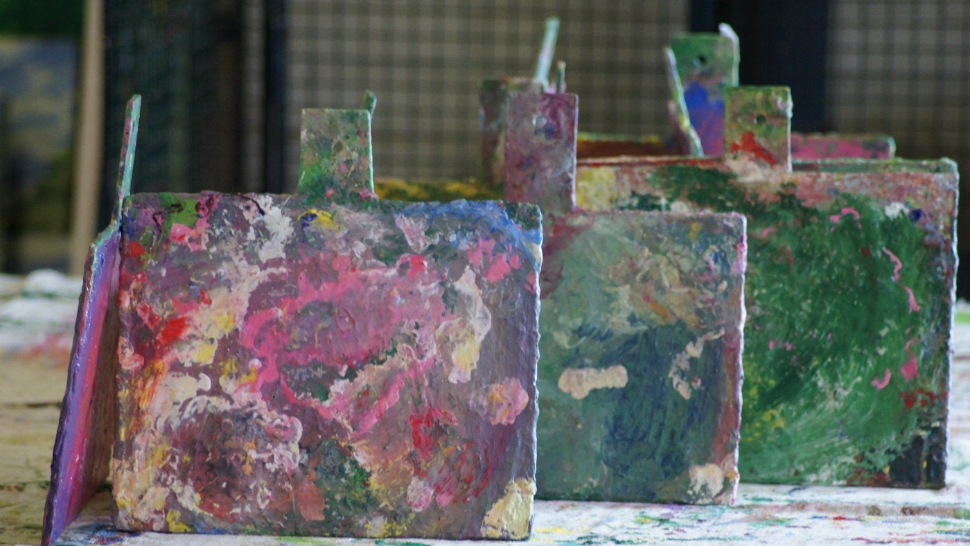 A row of easels lined up on a table and covered in paint