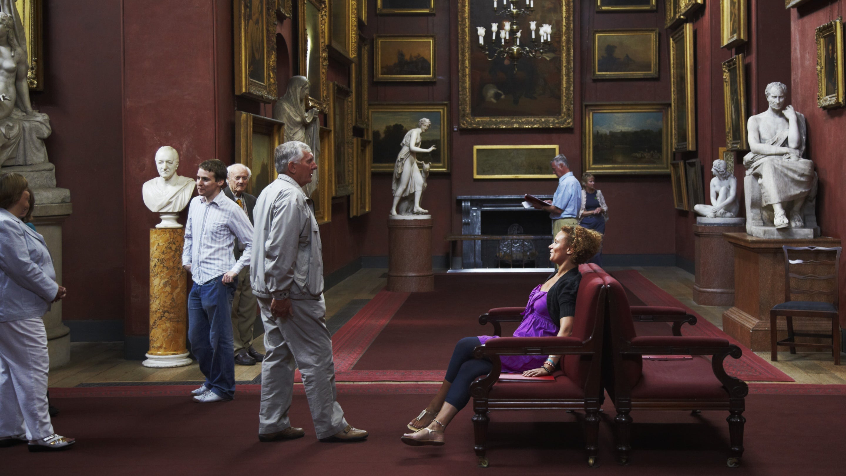 A group of visitors spread out in the North Gallery at Petworth House in West Sussex, looking at the paintings and objects on display.