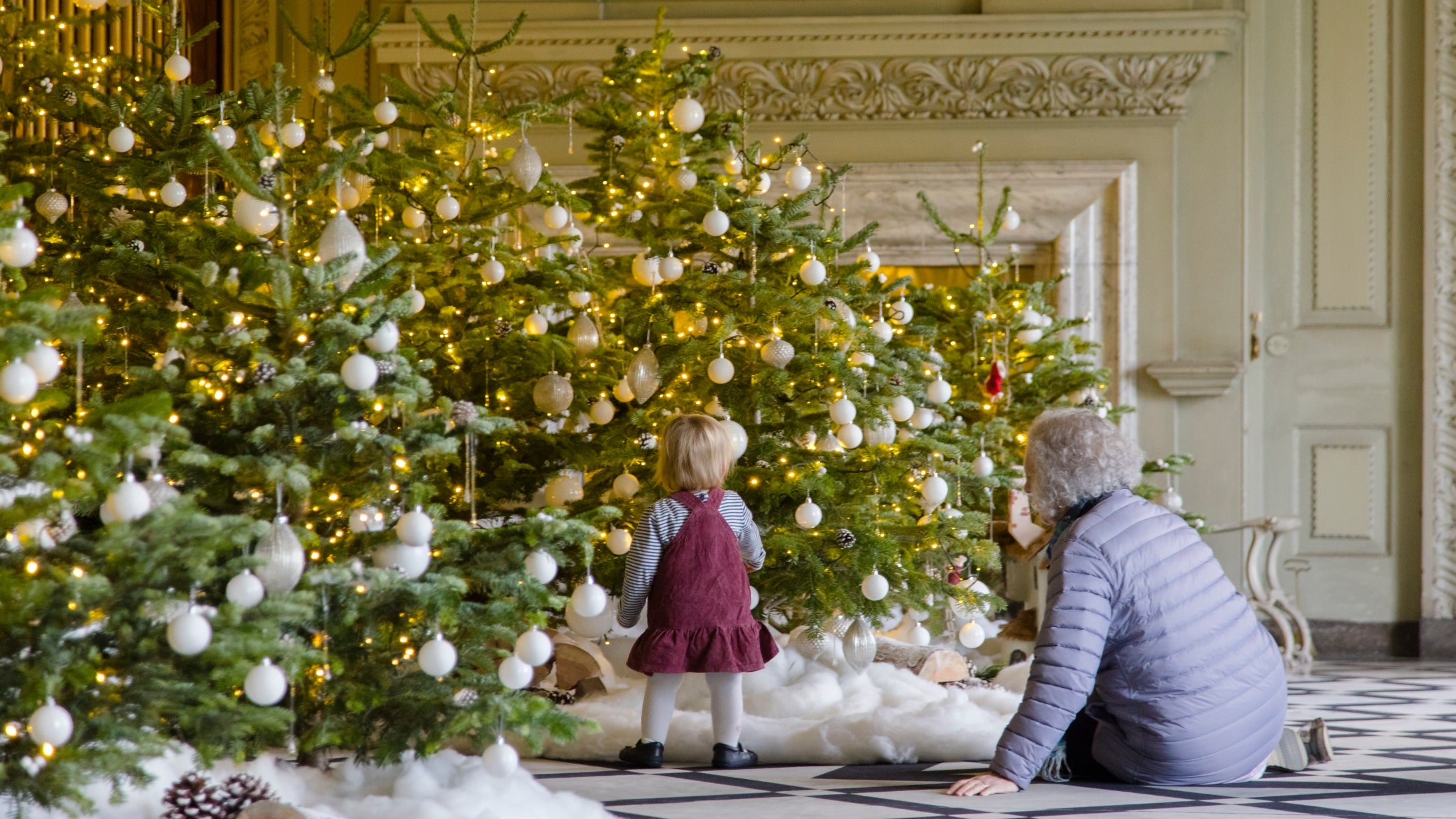 Little girl and grandparent admiring Christmas trees in Marble Hall, Petworth, West Sussex