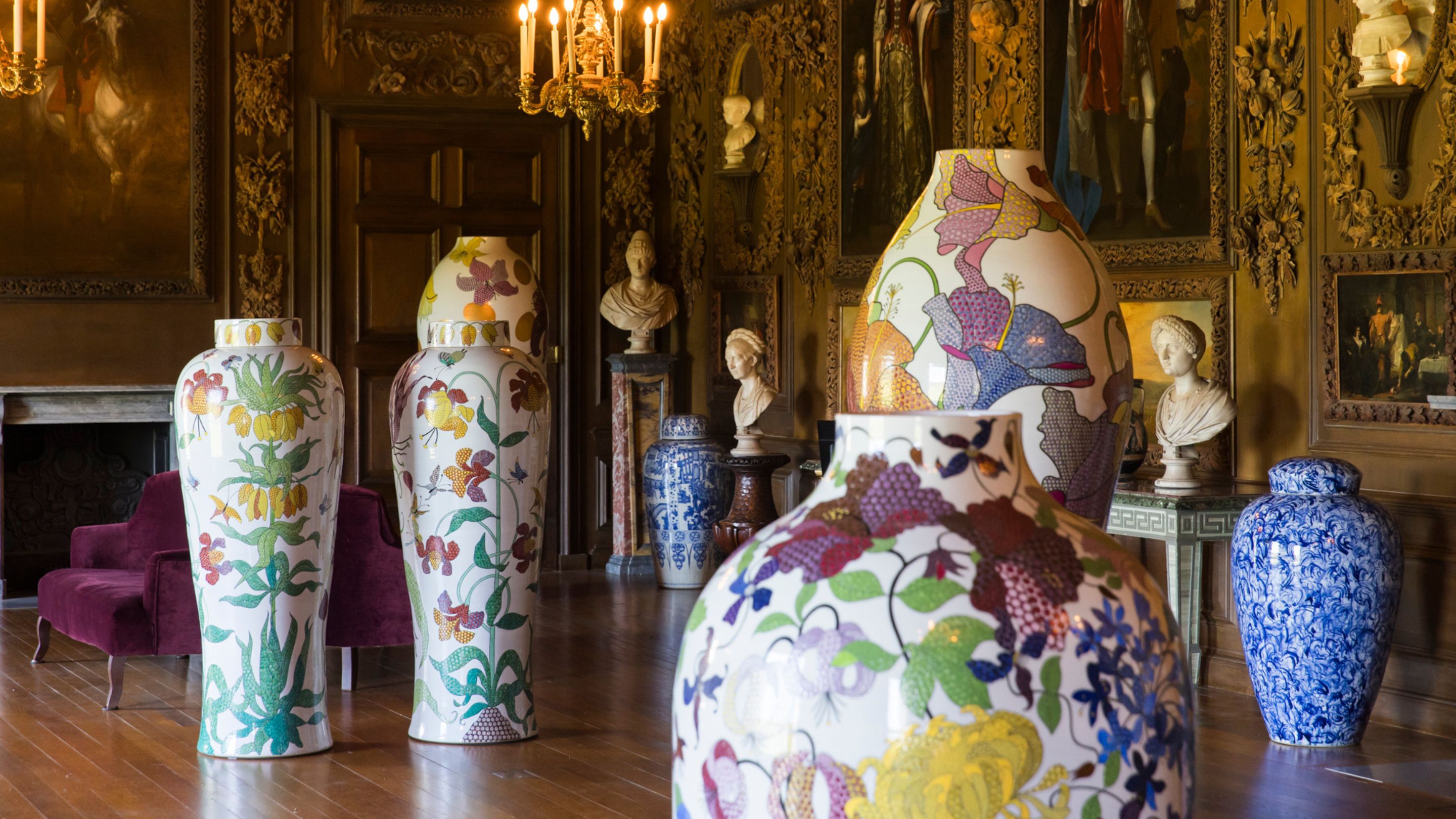 Large vases with colourful floral enamel decoration in Petworth's Carved Room against a backdrop of Grinling Gibbons wood carvings