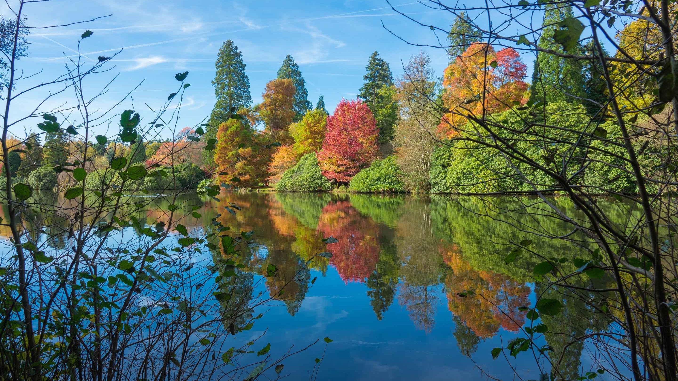 A view across the lake at Sheffield Park, East Sussex with the spectacular autumn colours of the trees perfectly reflected into the lake.
