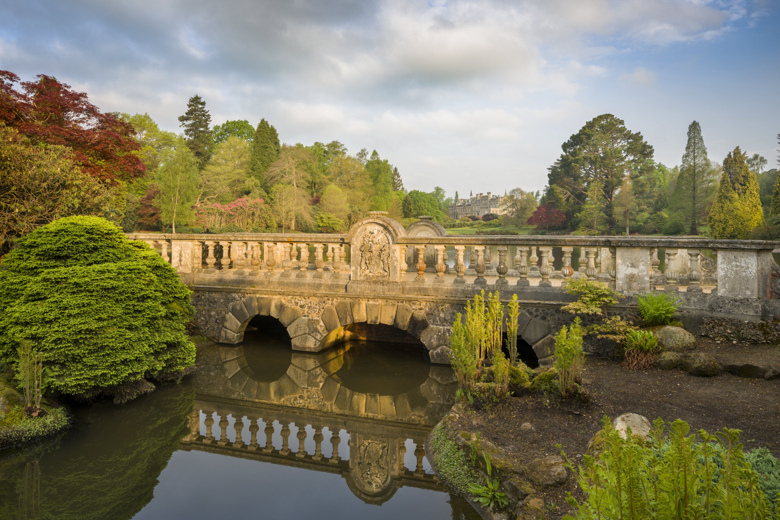 View across the water of First Bridge looking towards the house at Sheffield Park and Garden