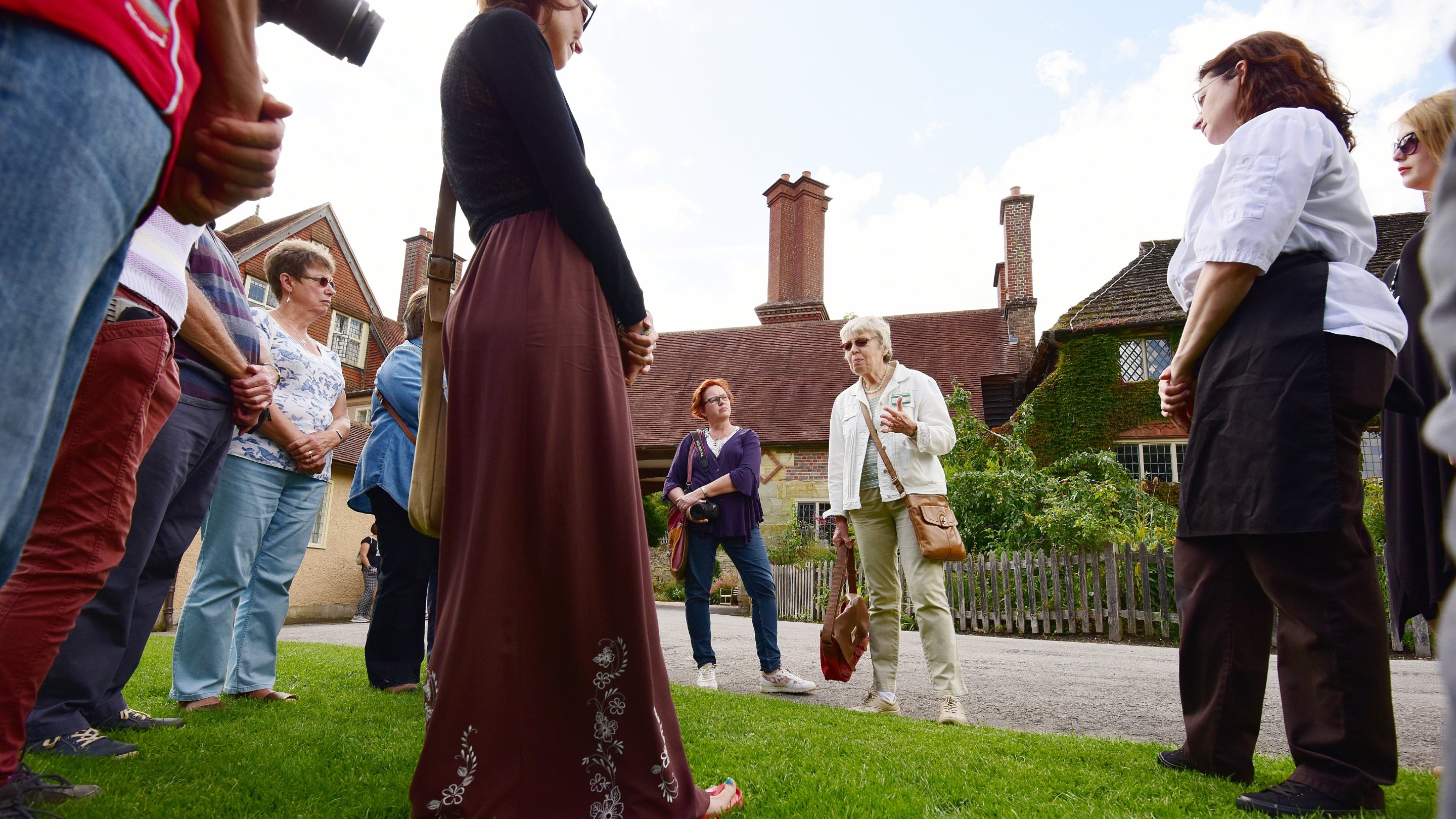 A group visit in front of Standen listening to a tour guide.