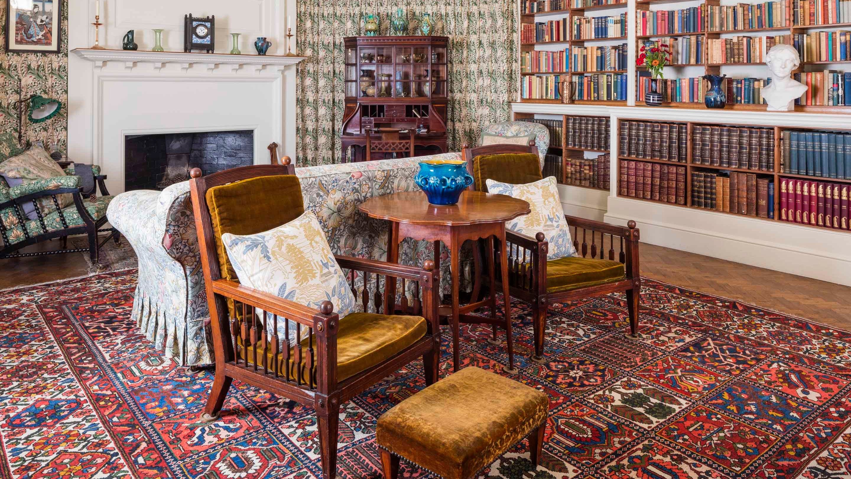 The Morning Room at Standen House, West Sussex, with a patterned carpet, two armchairs and bookshelves