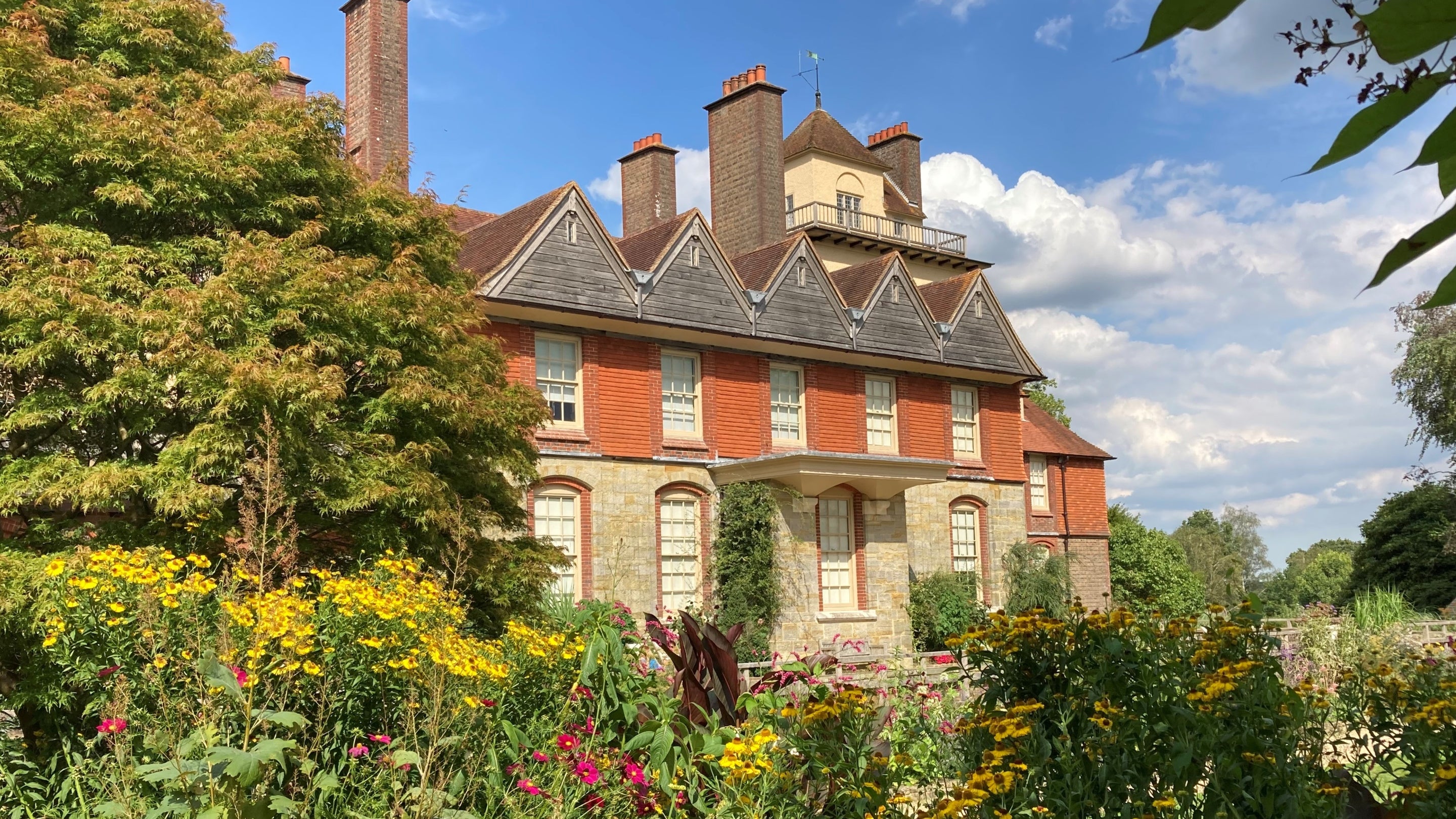 Looking at Standen from the garden in summertime with the house surrounded by flowers