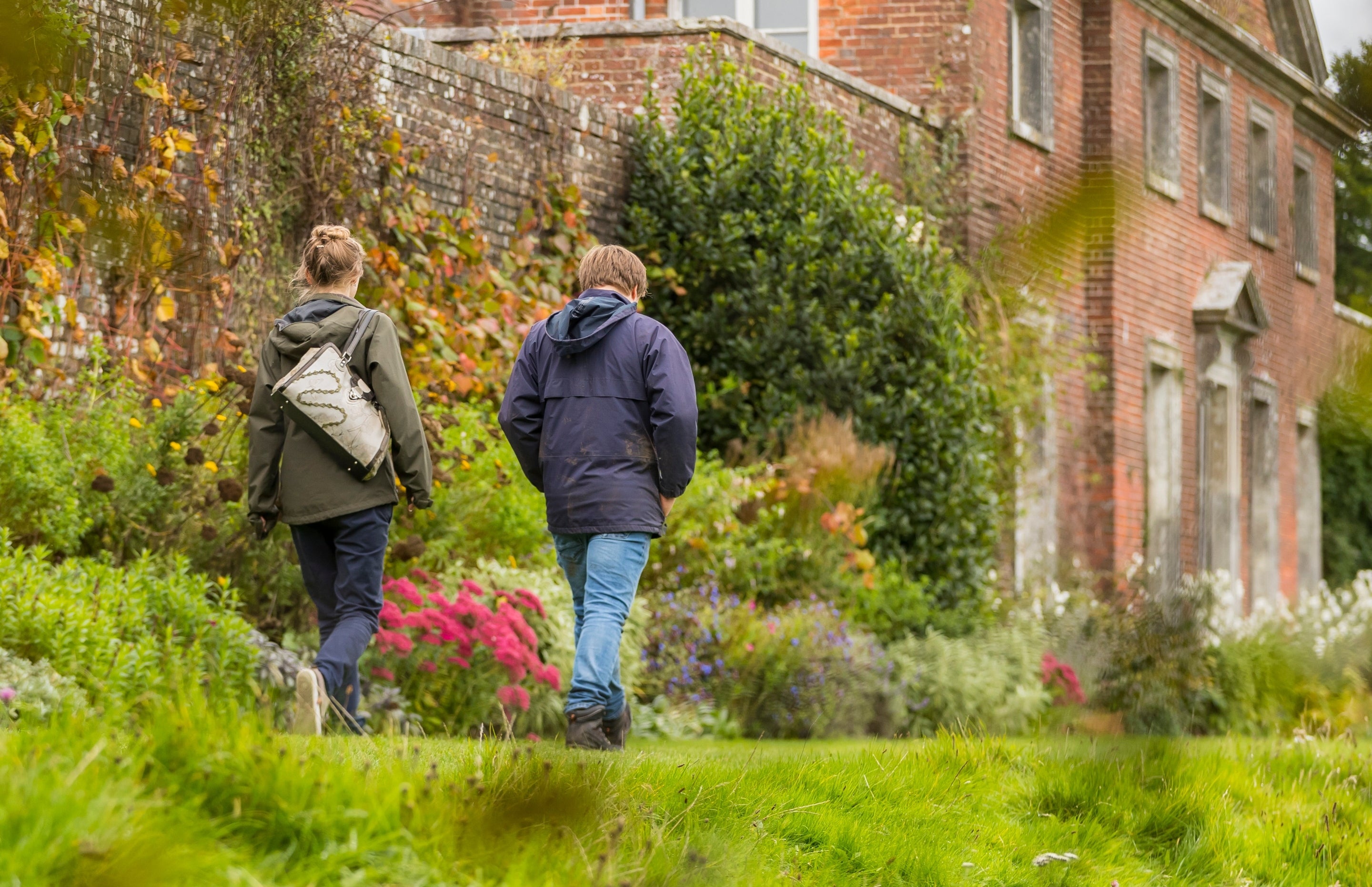 Visitors walking along flower border in autumn with exterior of house in background, Uppark, West Sussex
