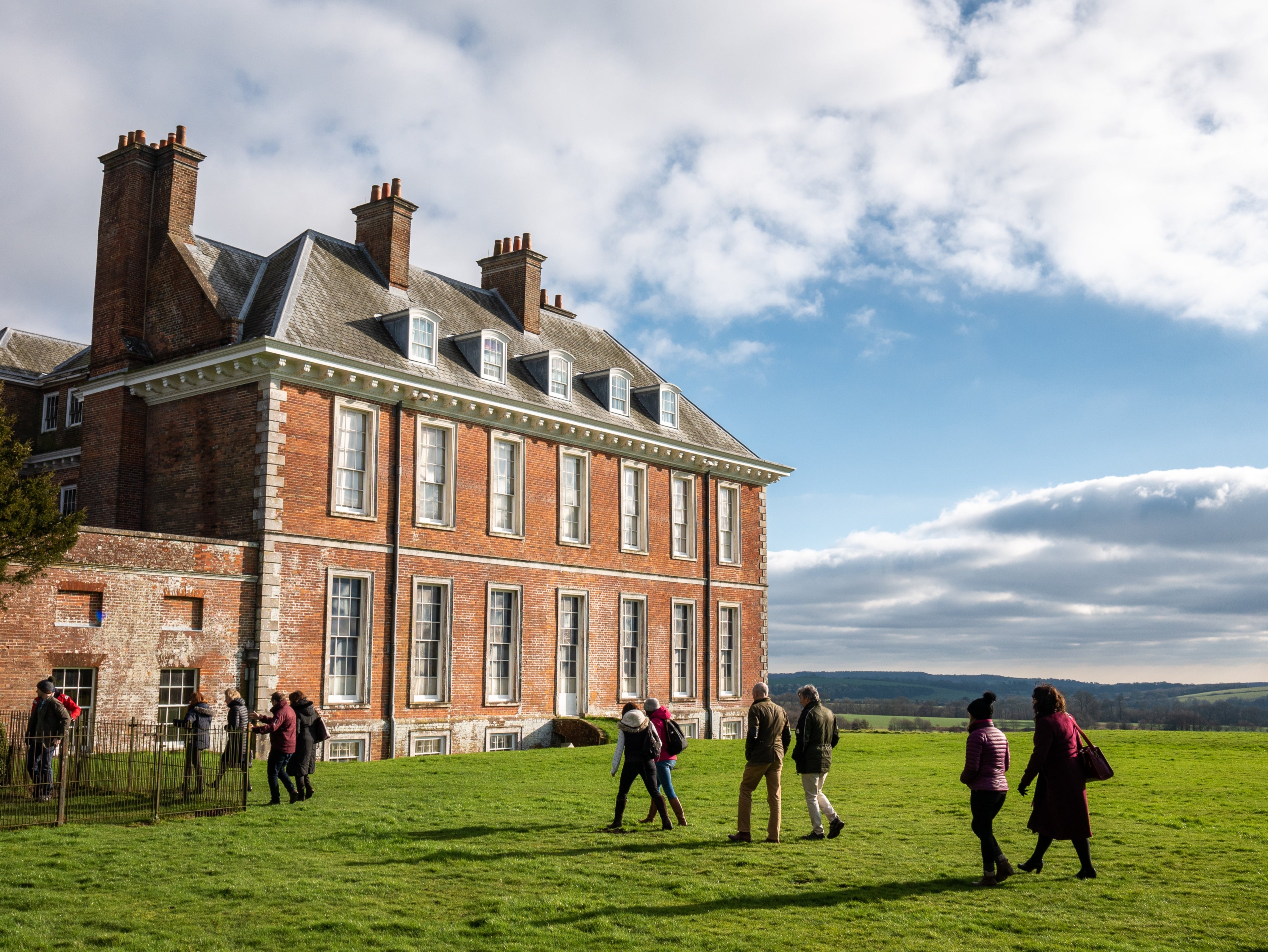 Visitors walking beside Uppark House, with countryside views and a bright autumn sky in the background.