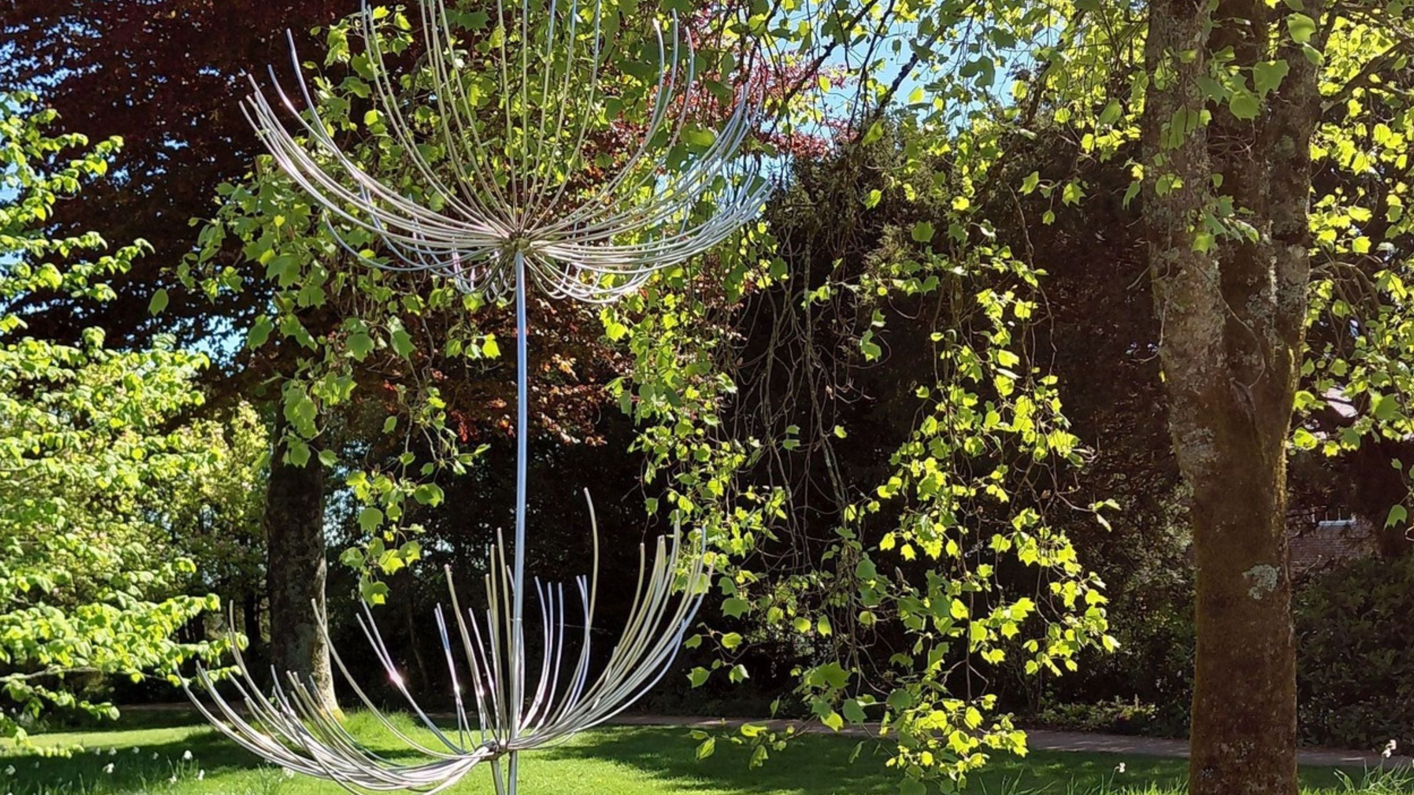 Wire garden sculpture on a lawn with trees behind, at Uppark