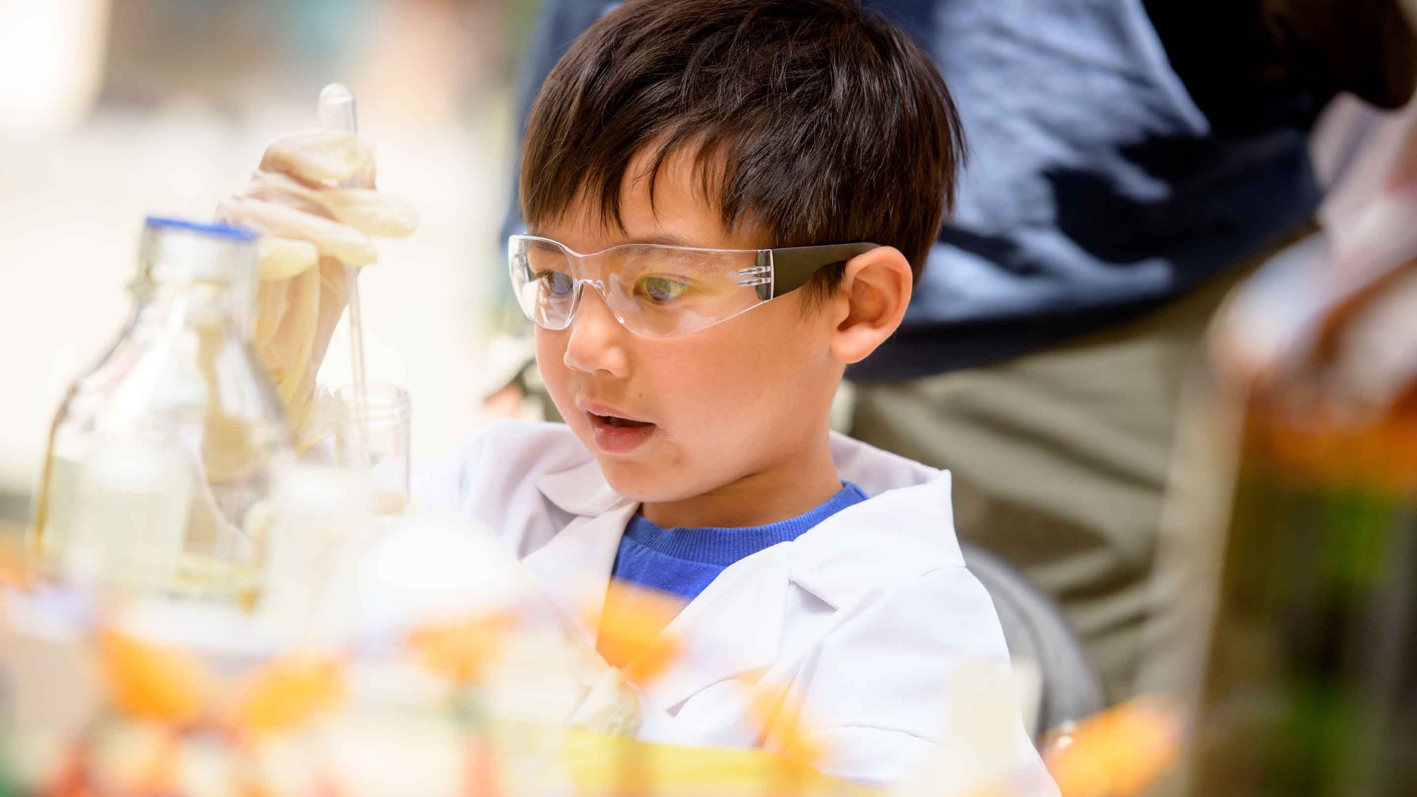 A child wearing safety goggles holds a test tube and a dropper at Wakehurst, West Sussex