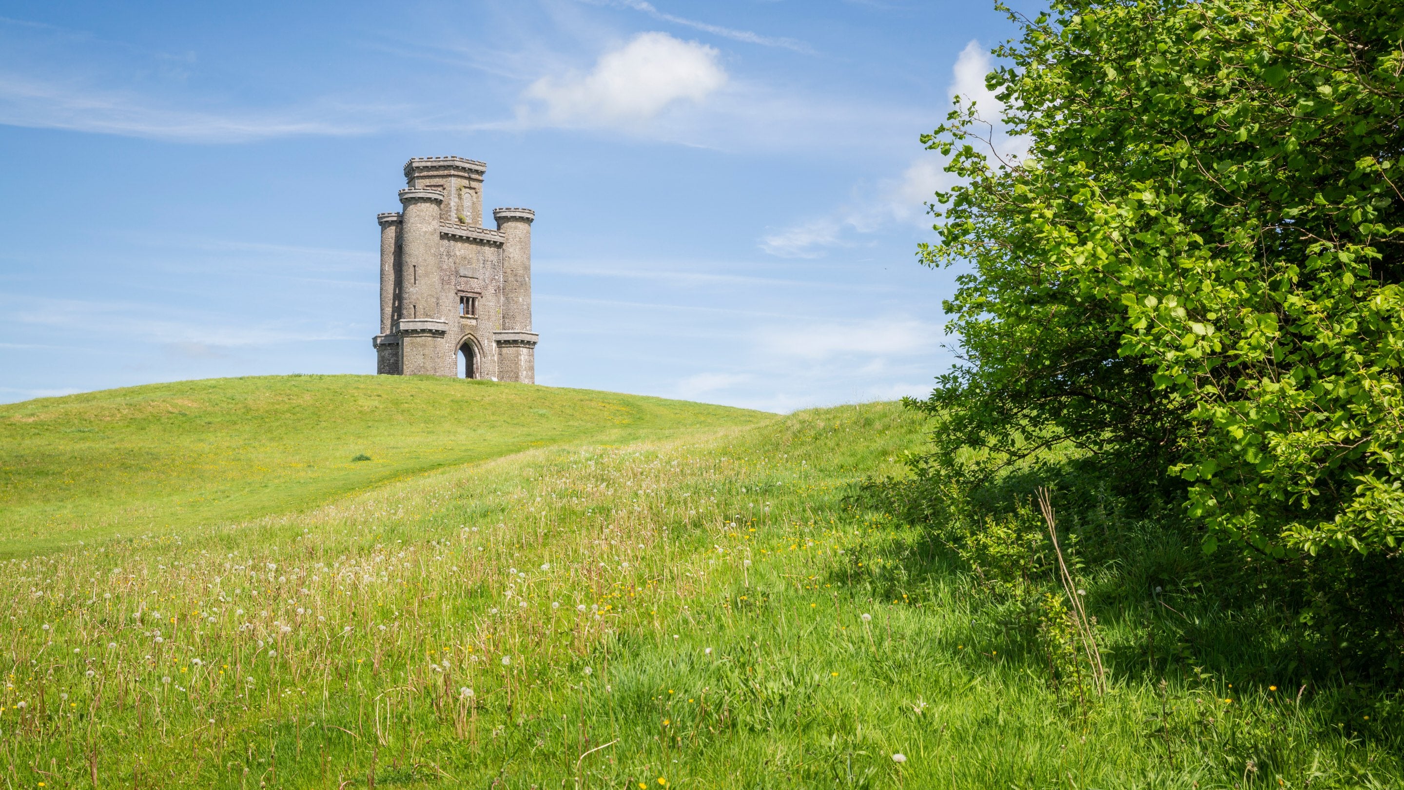 Tŵr Paxton, Sir Gâr, Cymru, ar dop bryn gydag awyr las a glaswelltir gwyllt yn y tu blaen.