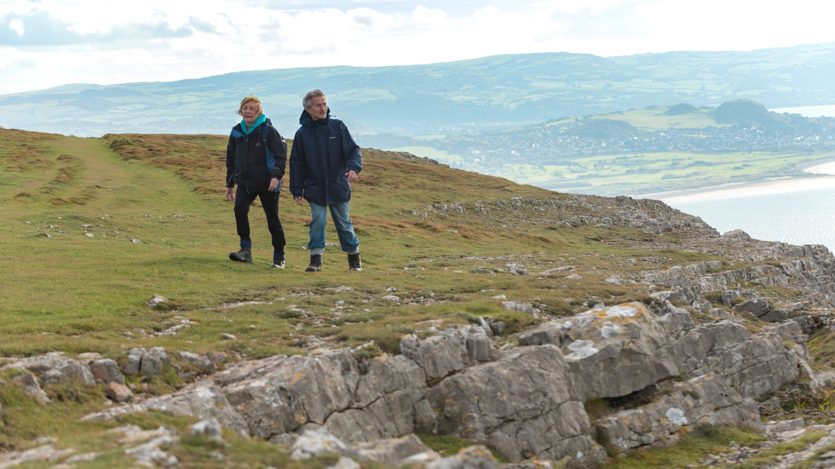 Ymwelwyr yn cerdded ar Ben y Gogarth, Gogledd Cymru, gyda golygfa o’r arfordir