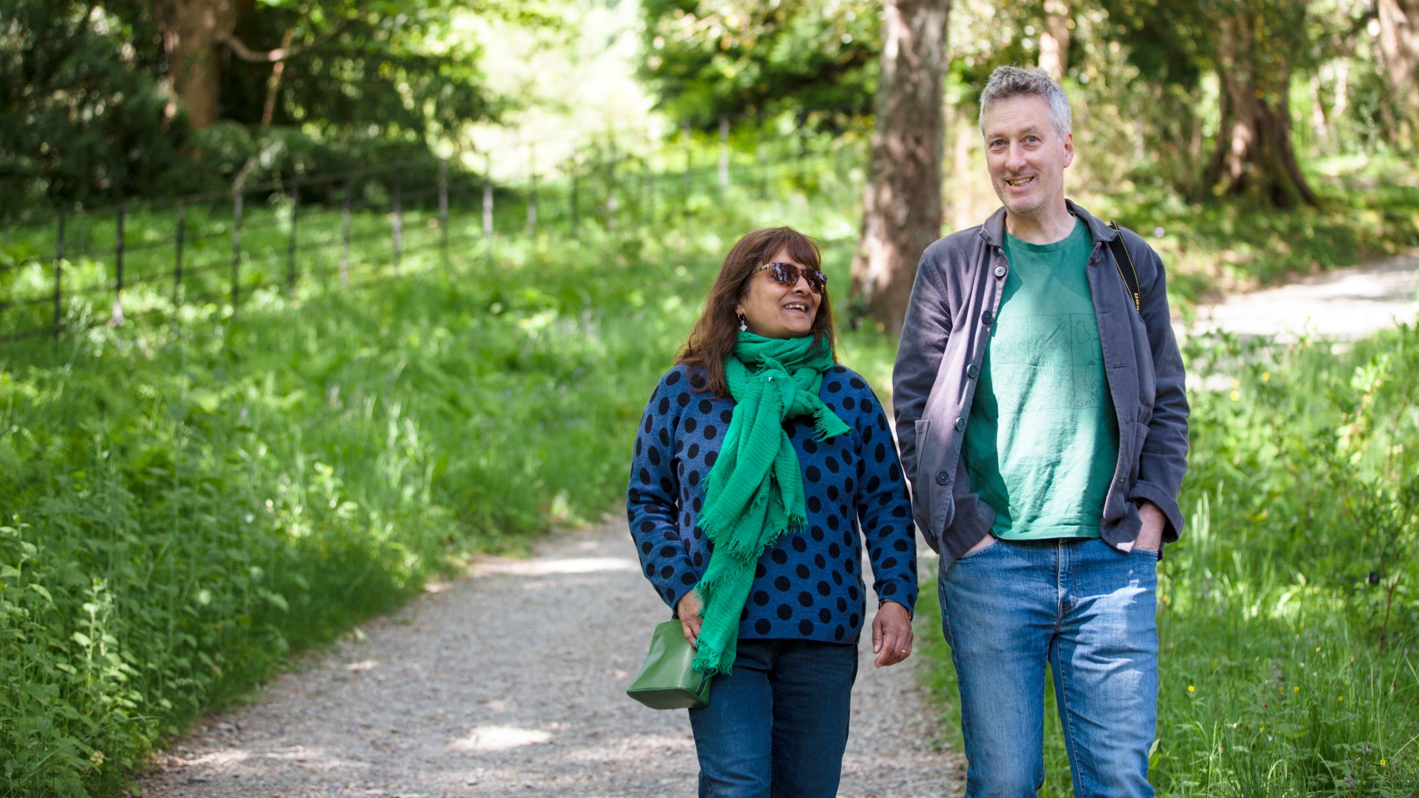 A couple walk along a track bounded by grass and trees in the Arboretum, Bodnant Garden, Conwy, Wales