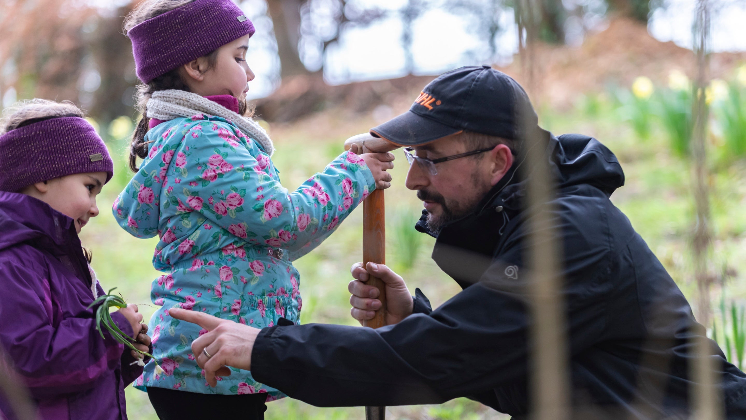 Children in winter clothing helping a gardener at Bodnant to plant snowdrops