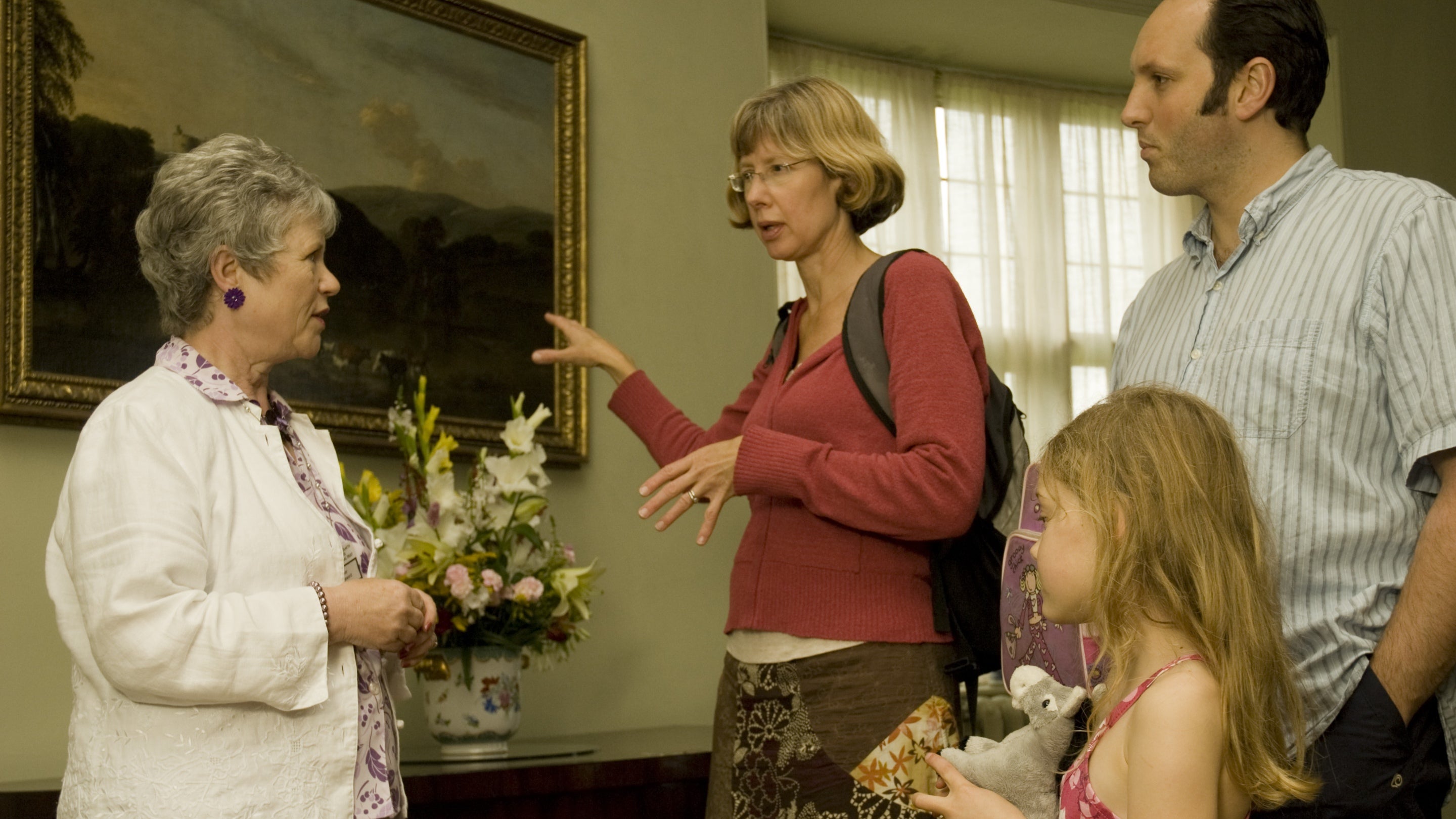 Tywysydd ystafell gwirfoddol a theulu gyda phaentiad a blodau yn y cefndir yng Nghastell y Waun, Wrecsam, Cymru