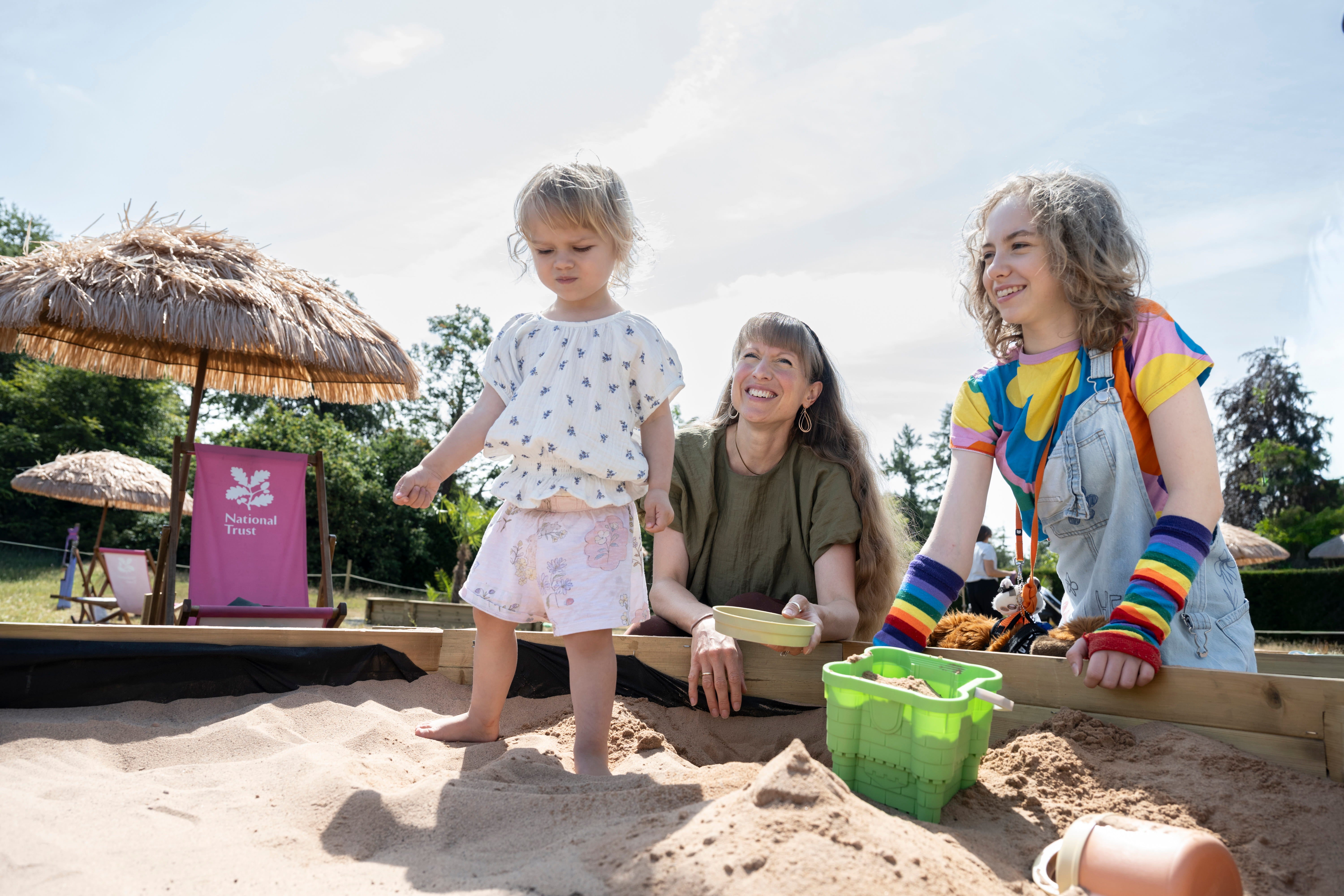 A young child playing in a sandpit with family members at Chirk Castle.