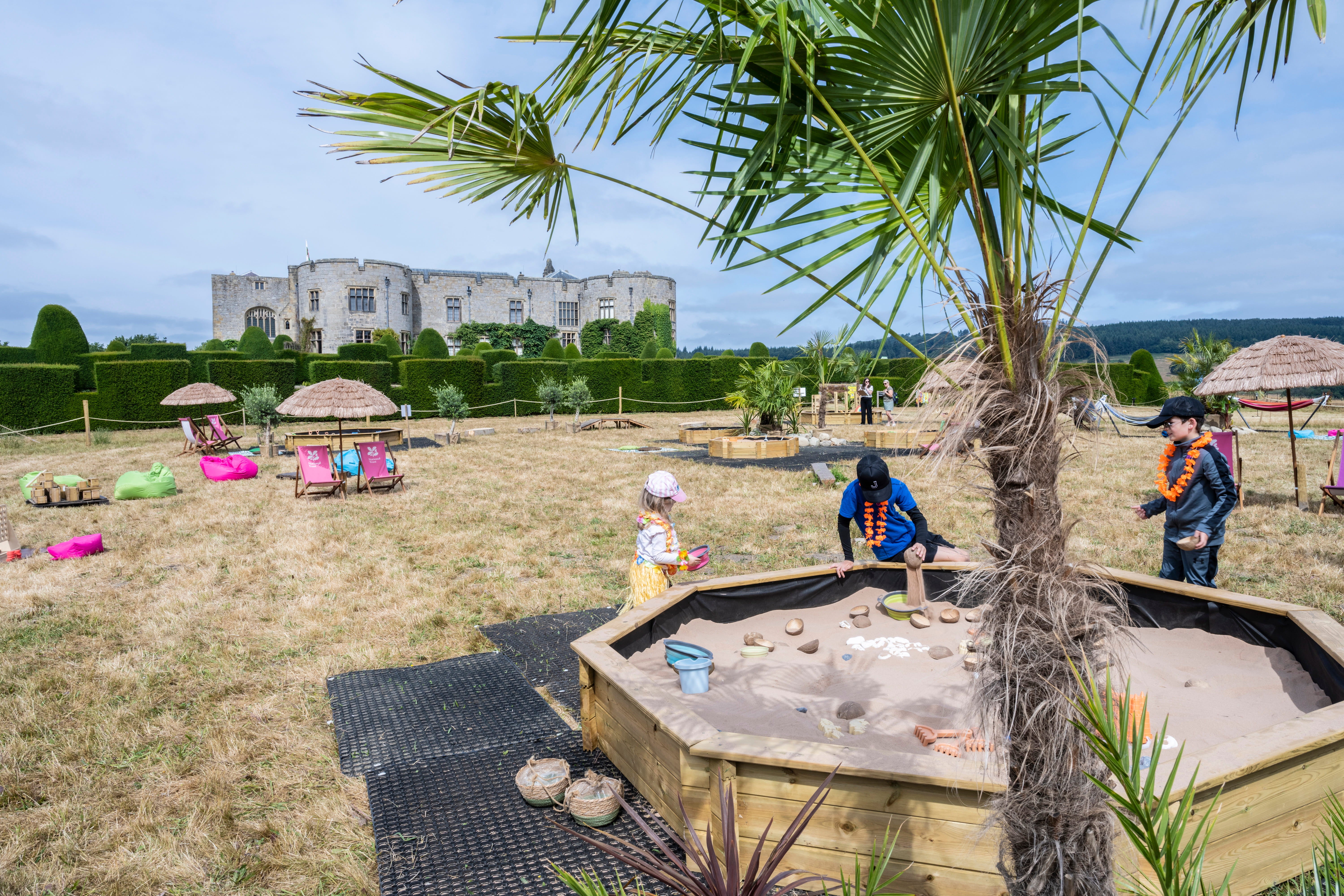 Children playing in a large sandpit surrounded by summer activities in the garden at Chirk Castle.