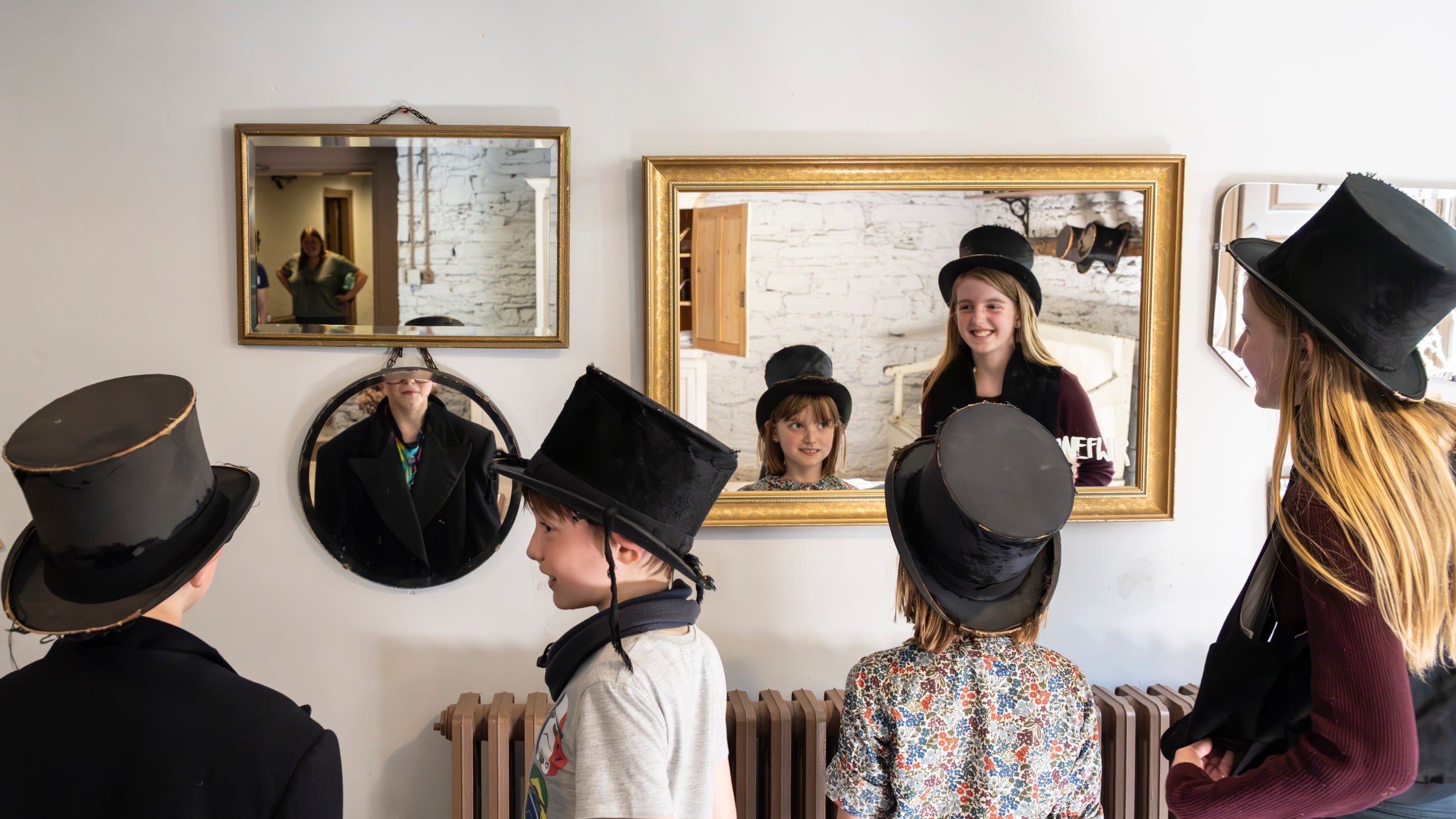 Several children trying on hats and looking at themselves in mirrors on the wall
