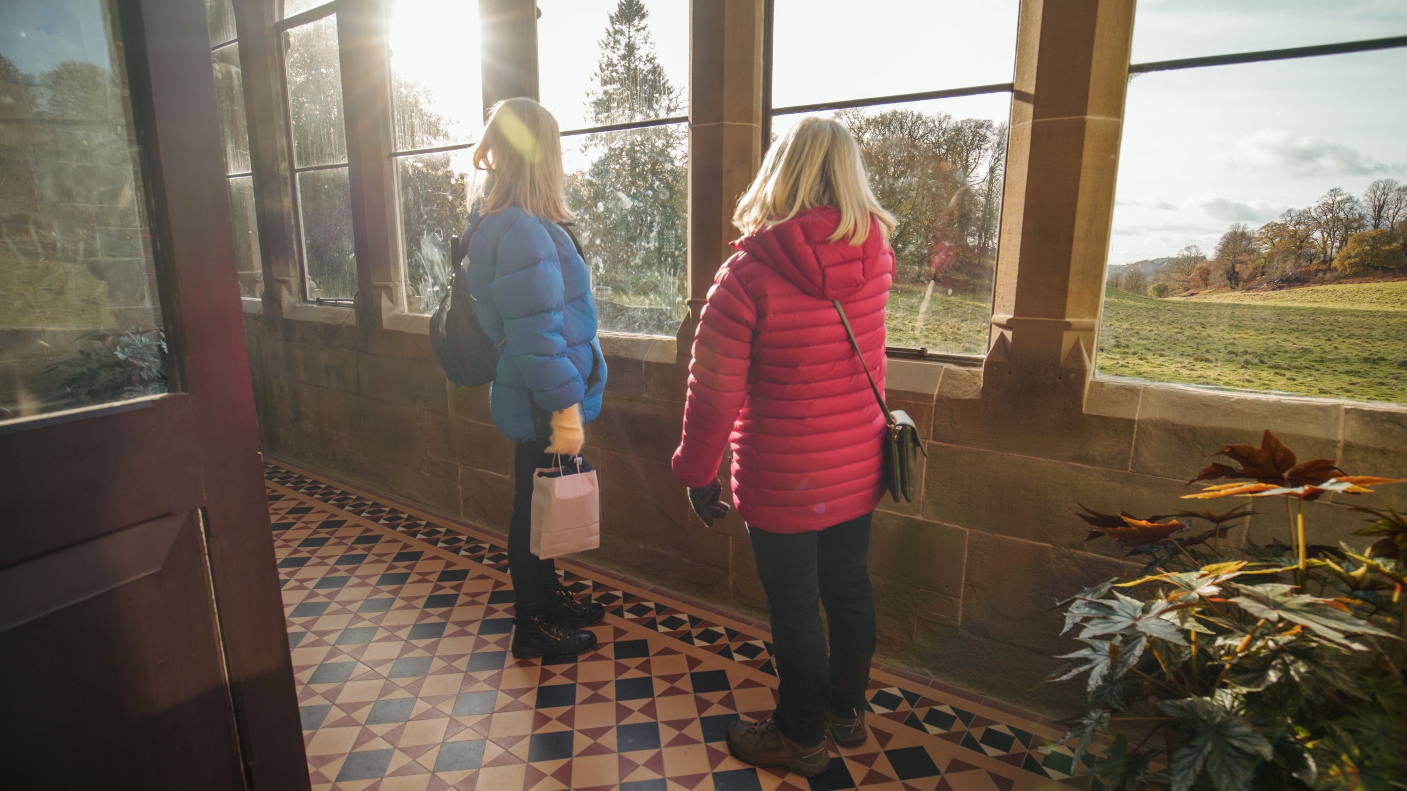 Two people looking through the conservatory windows on the first floor of Newton House out towards the Deer Park, Dinefwr, Carmarthenshire