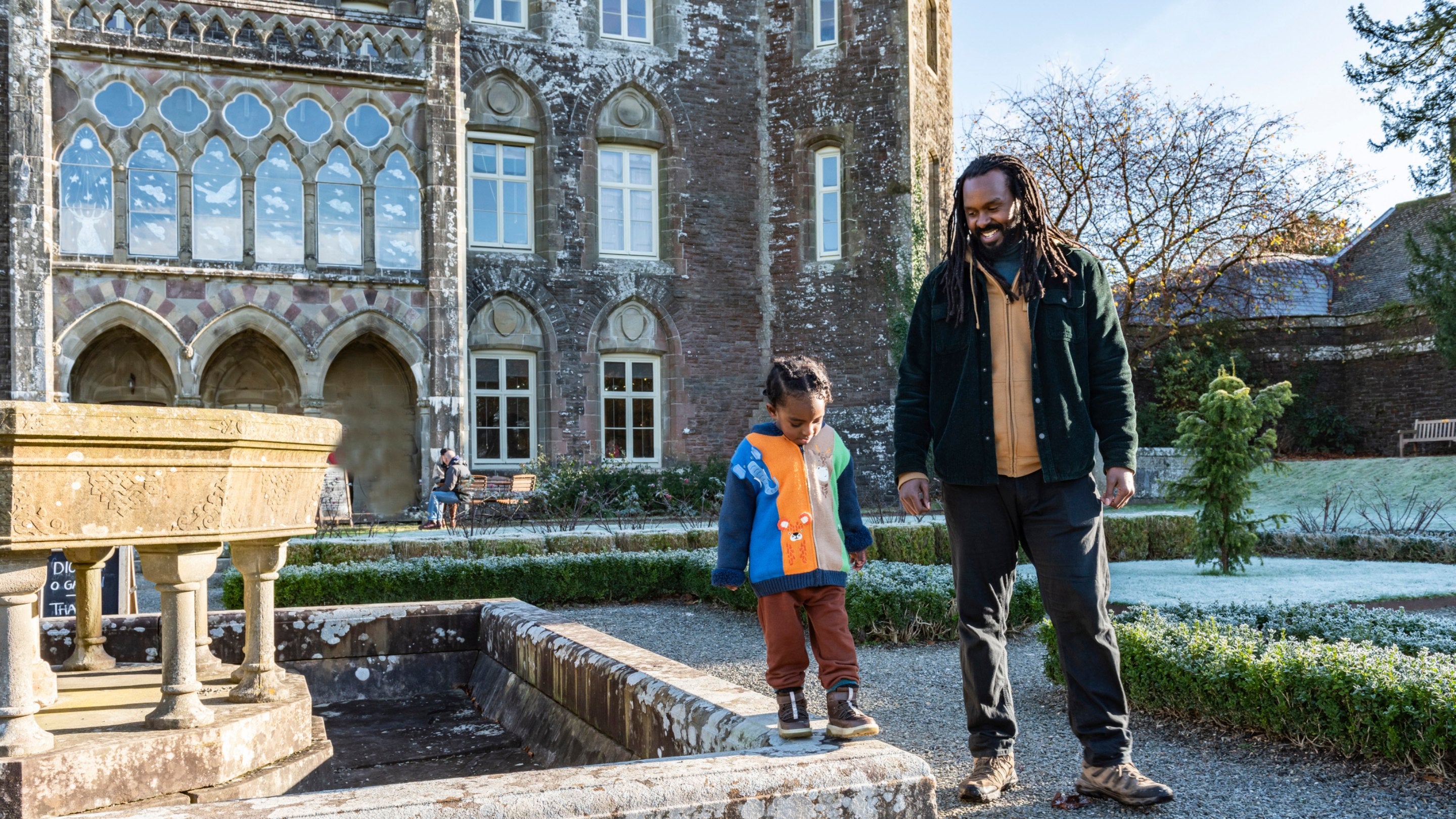 Man and child in the frosty gardens, the background is the building and there are parts of small green hedges in the gardens