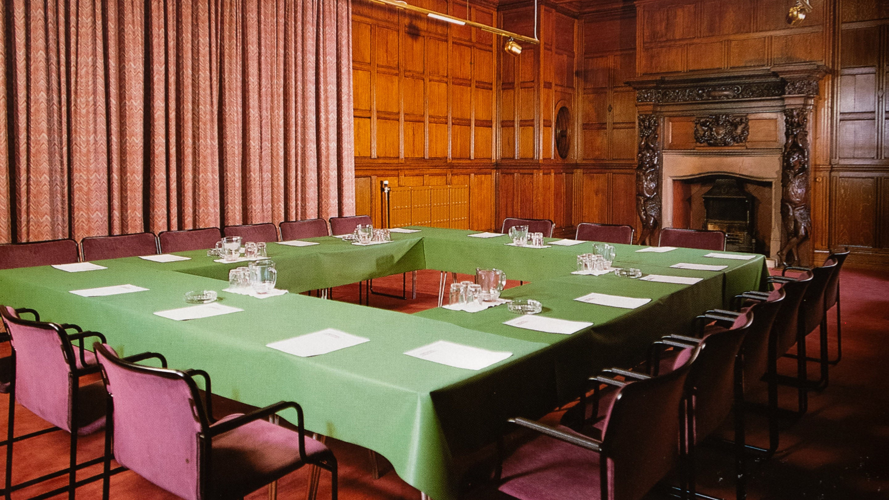 Bwrdd a chadeiriau’r ganolfan gynadledda yn yr Ystafell Dderw â’i phaneli pren yn y tŷ yng Ngerddi Dyffryn