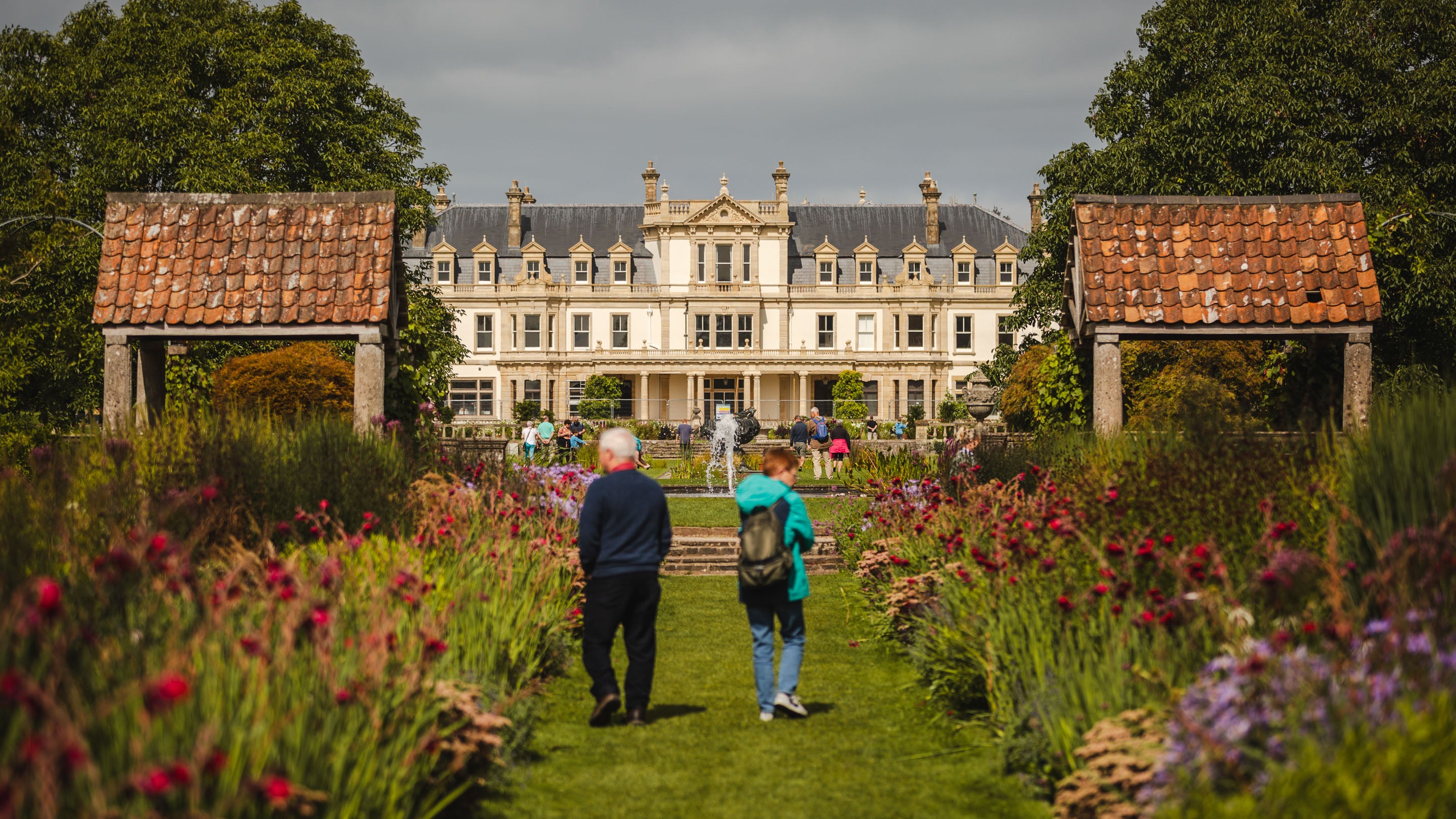 Golygfa o’r tŷ wedi’i adfer yn y pellter o’r gerddi gyda blodau yn y blaendir yng Ngerddi Dyffryn