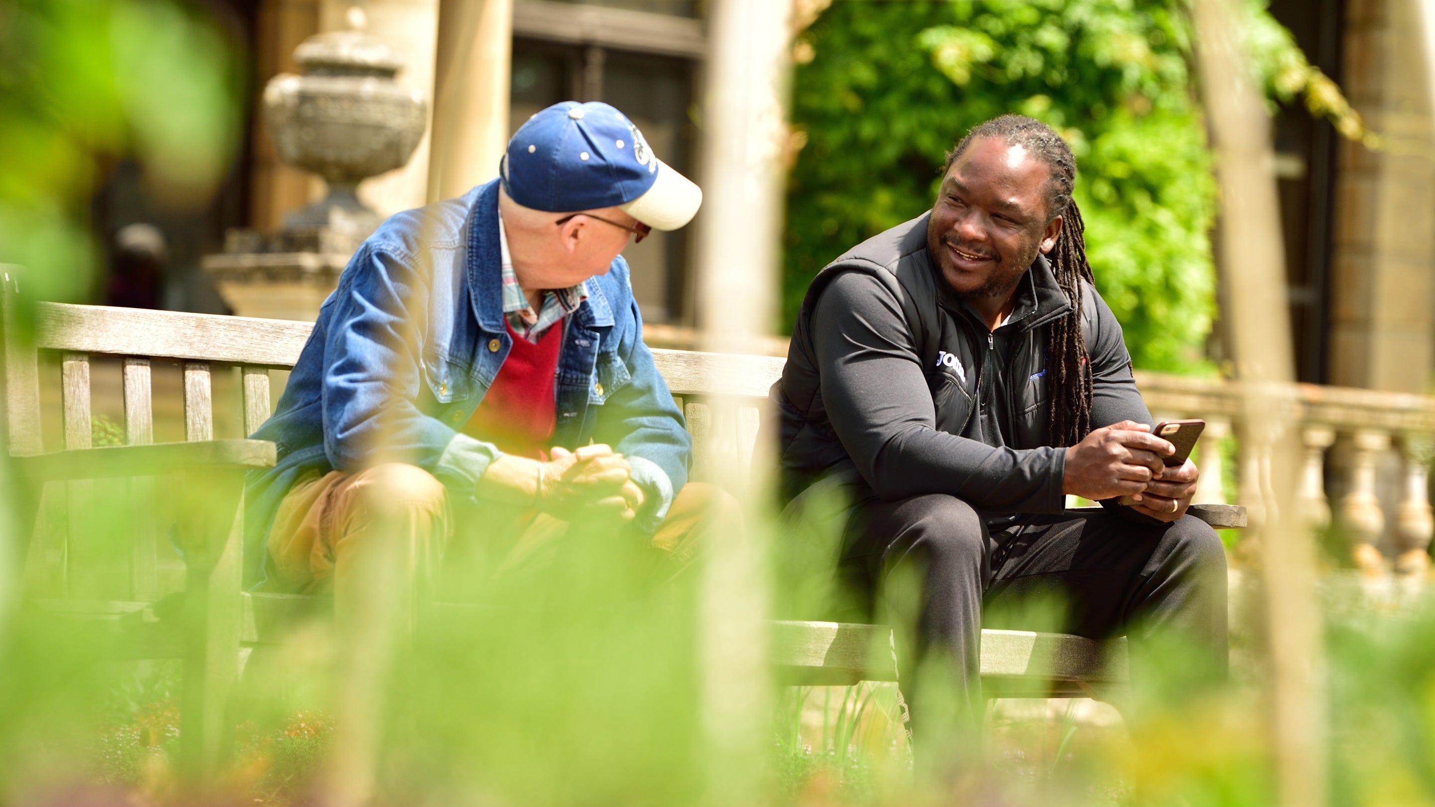 Two visitors sit on a bench chatting surrounded by spring greenery