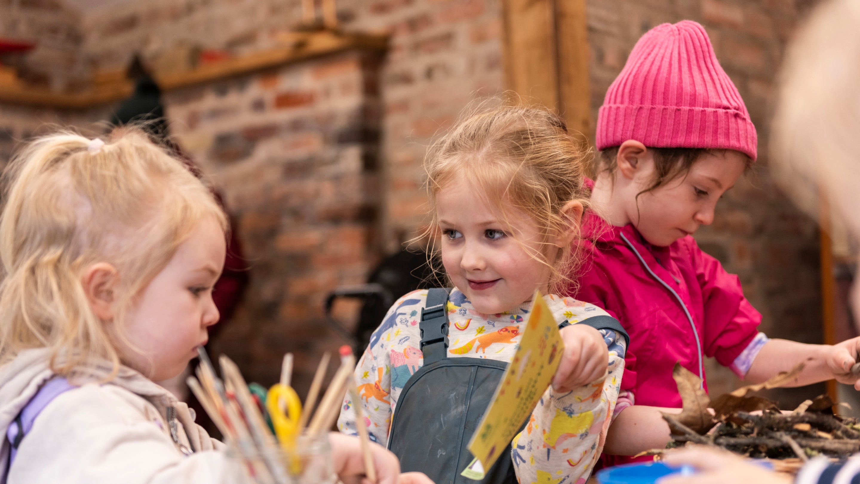 Three children taking part in crafts at a table, including paper, card and sticks