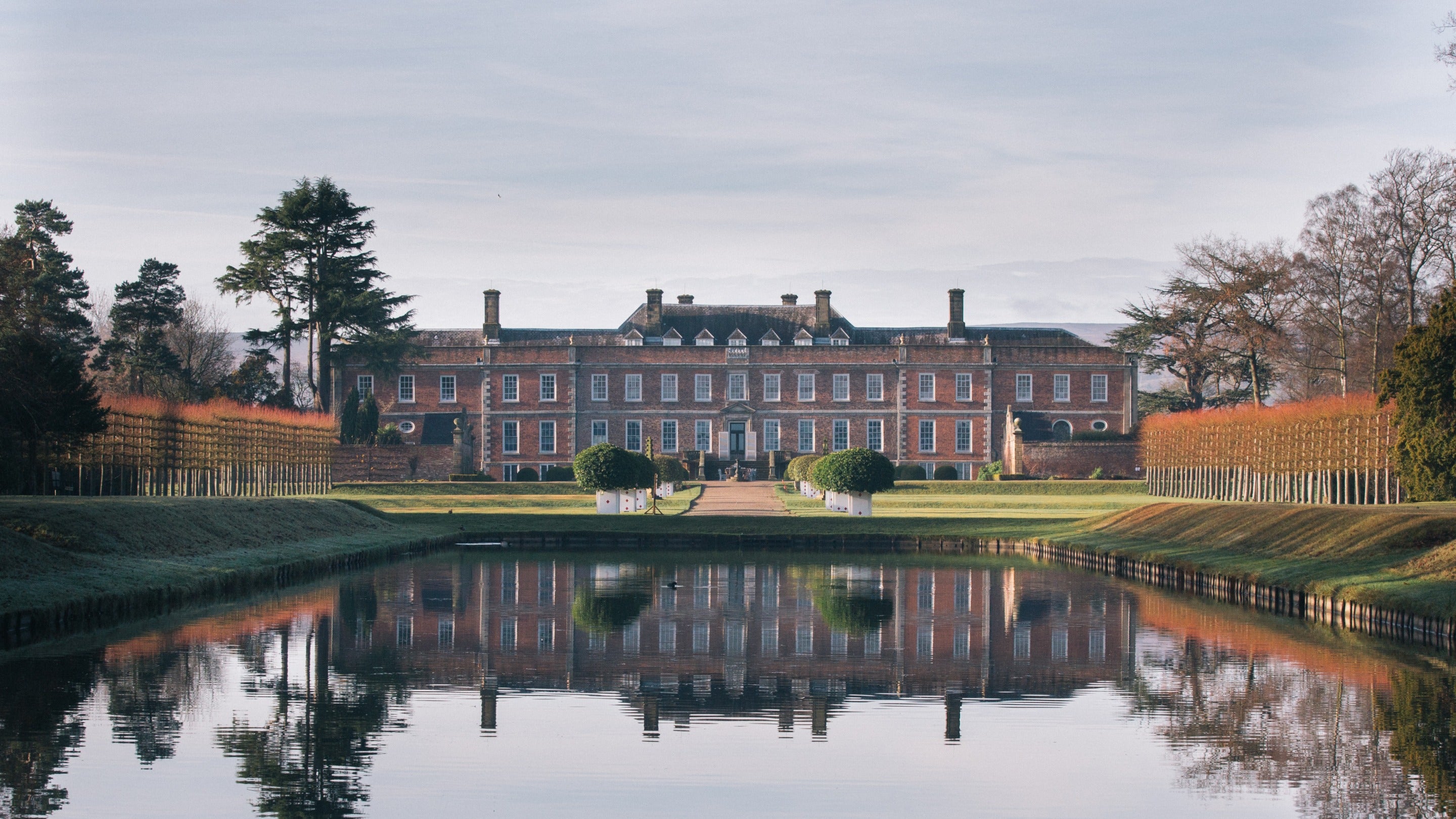 Golygfa ar draws y llyn tuag at y tŷ yn Erddig, Clwyd, sy’n cael ei adlewyrchu ar y dŵr.